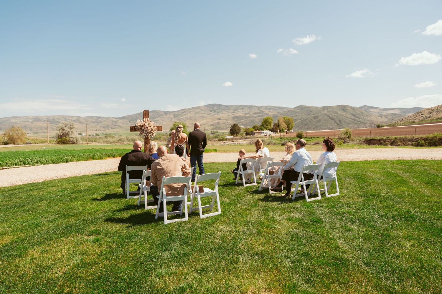 White chairs arranged on green grass for outdoor wedding ceremony with mountains in background.