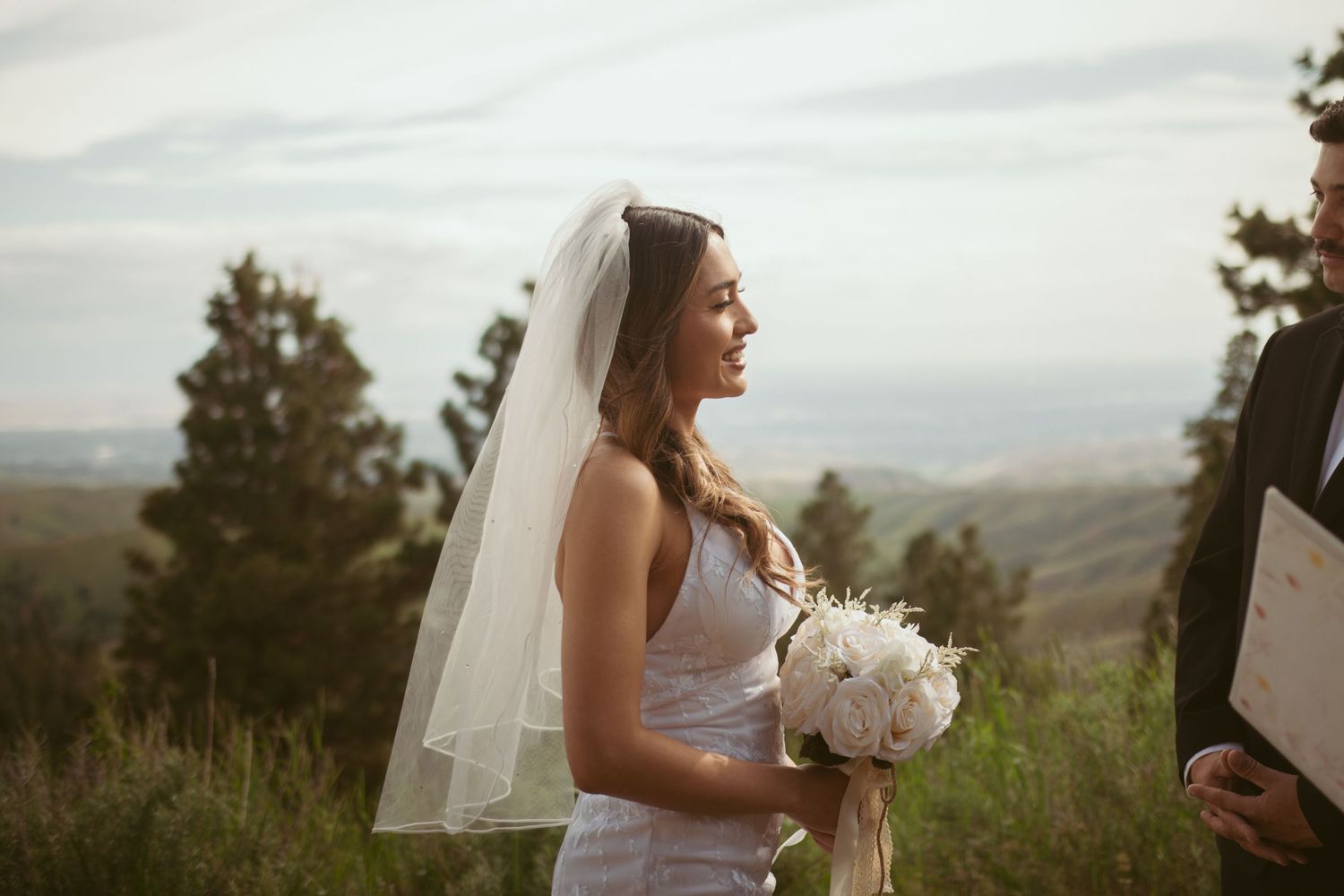 Couple sharing a romantic moment on a hilltop surrounded by pine trees.