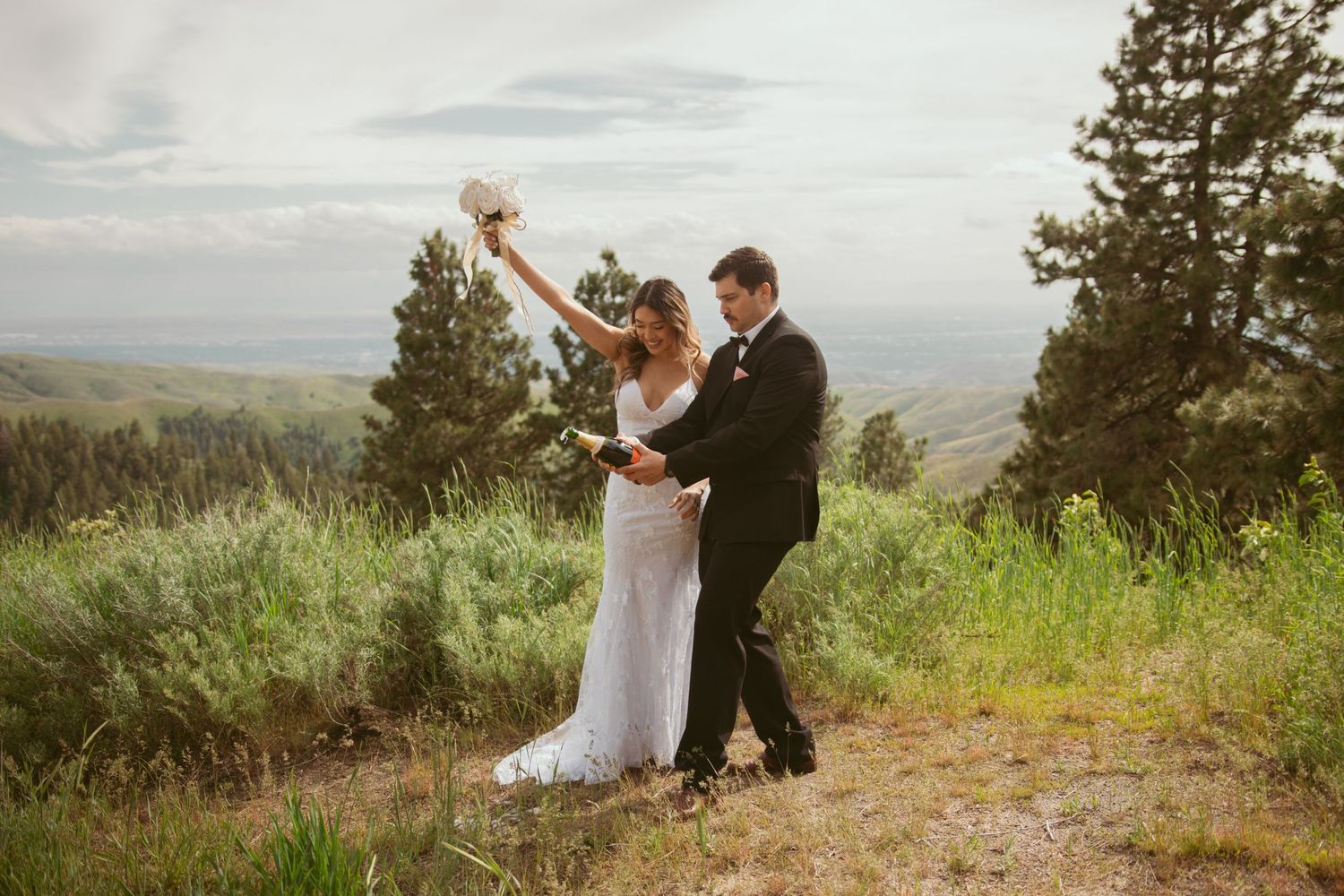 Wedding couple enjoys champagne while overlooking a scenic mountain valley landscape.