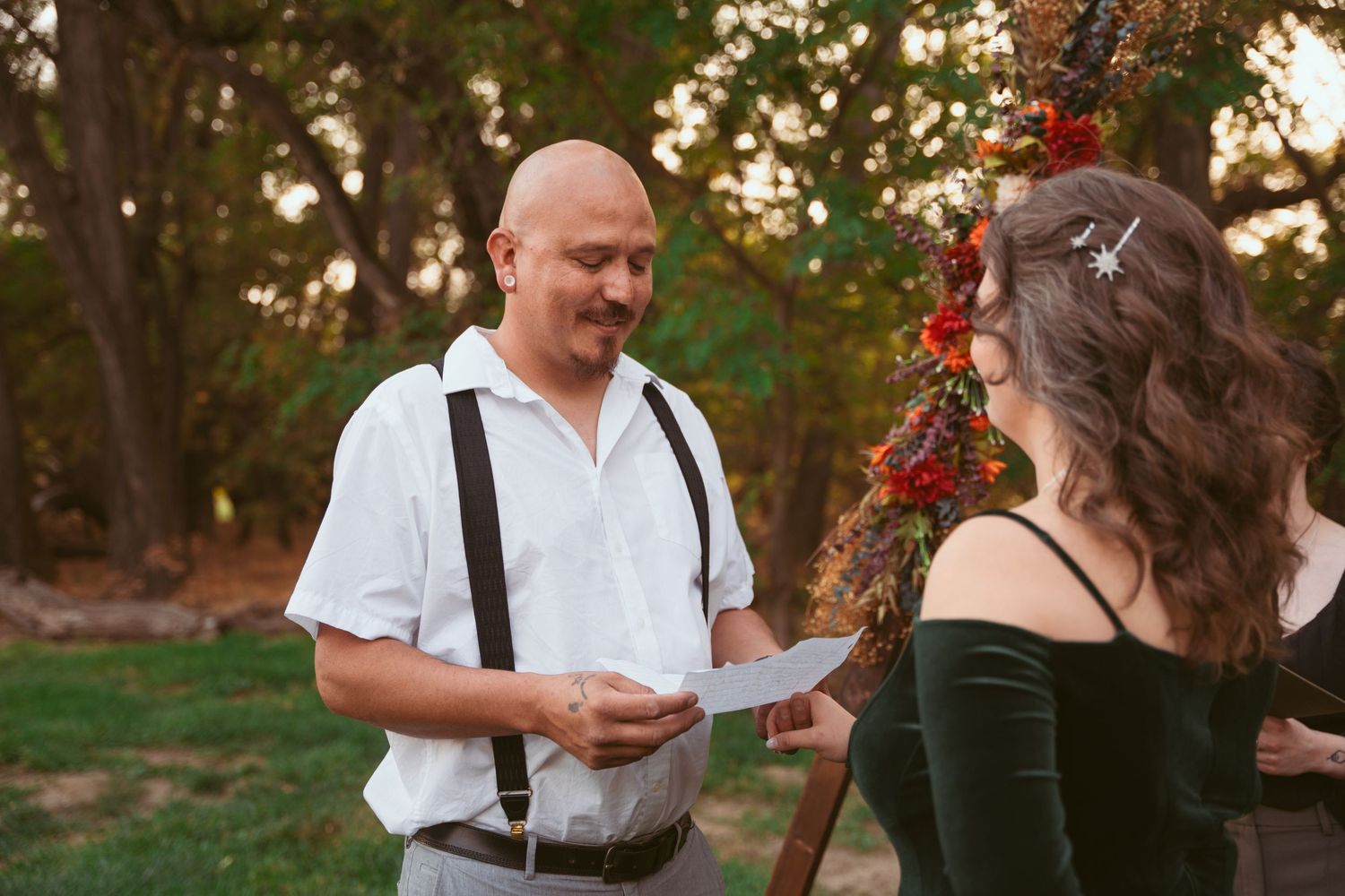 A couple exchanges heartfelt vows under autumn trees during their wedding ceremony.