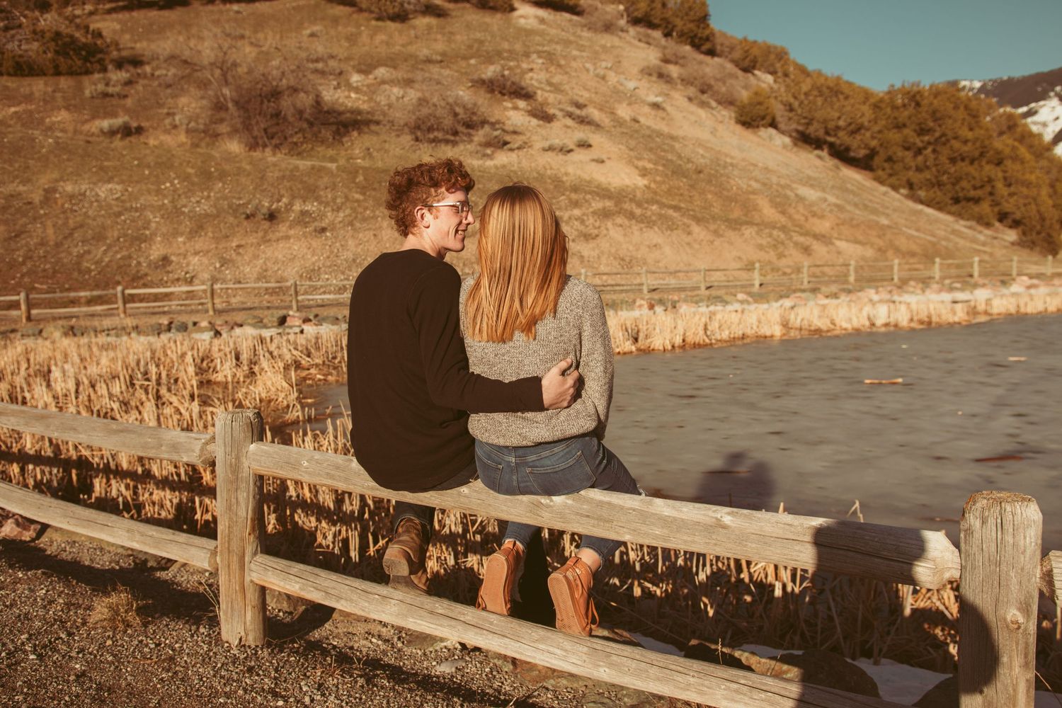 Couple sits together on wooden pier overlooking scenic mountain lake at sunset.