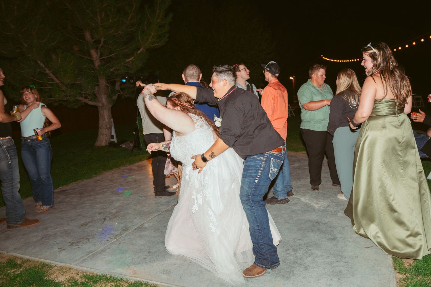 Couples dancing together at an outdoor evening wedding reception with string lights overhead.