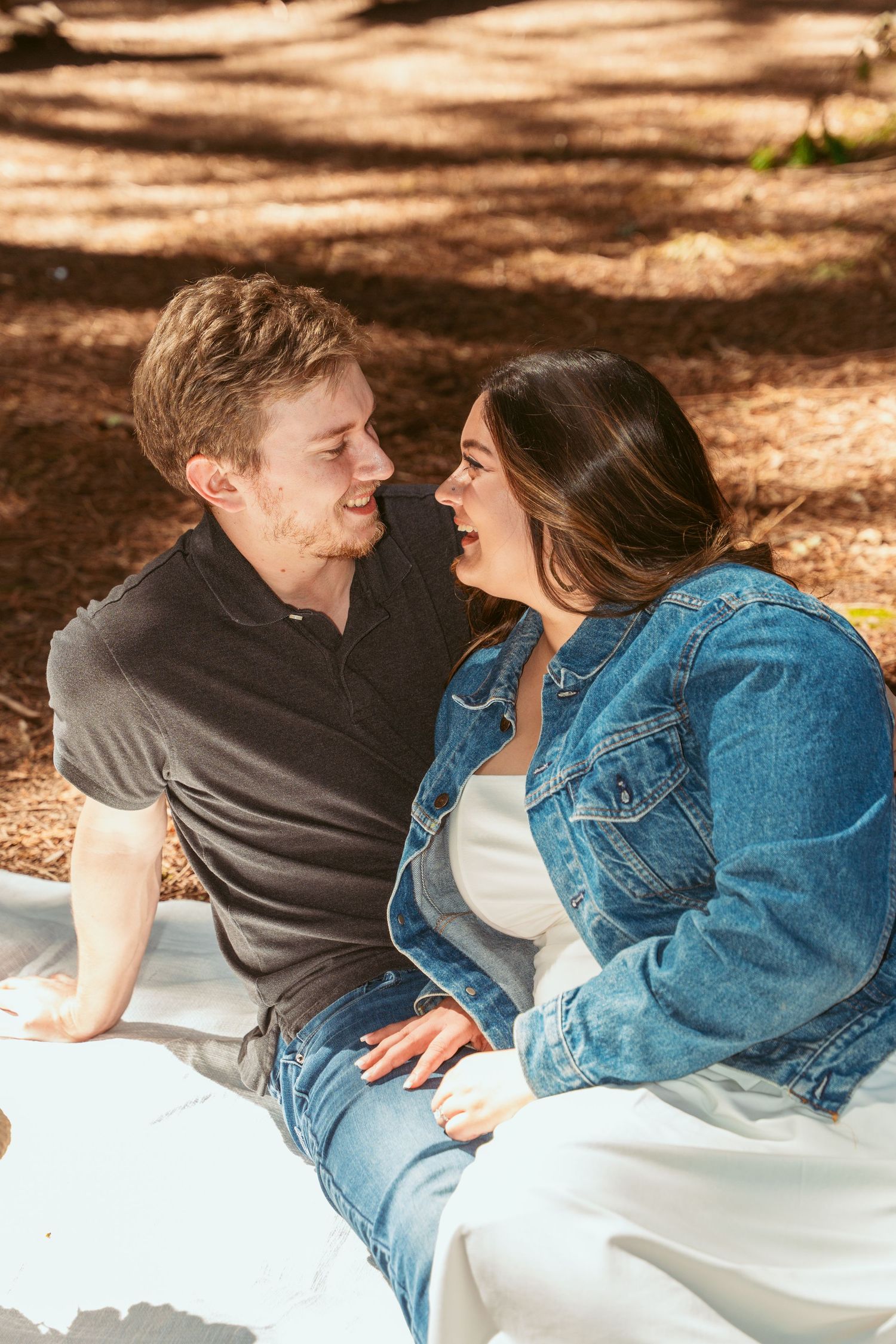 Couple relaxing on white blanket in a sunlit forest setting.