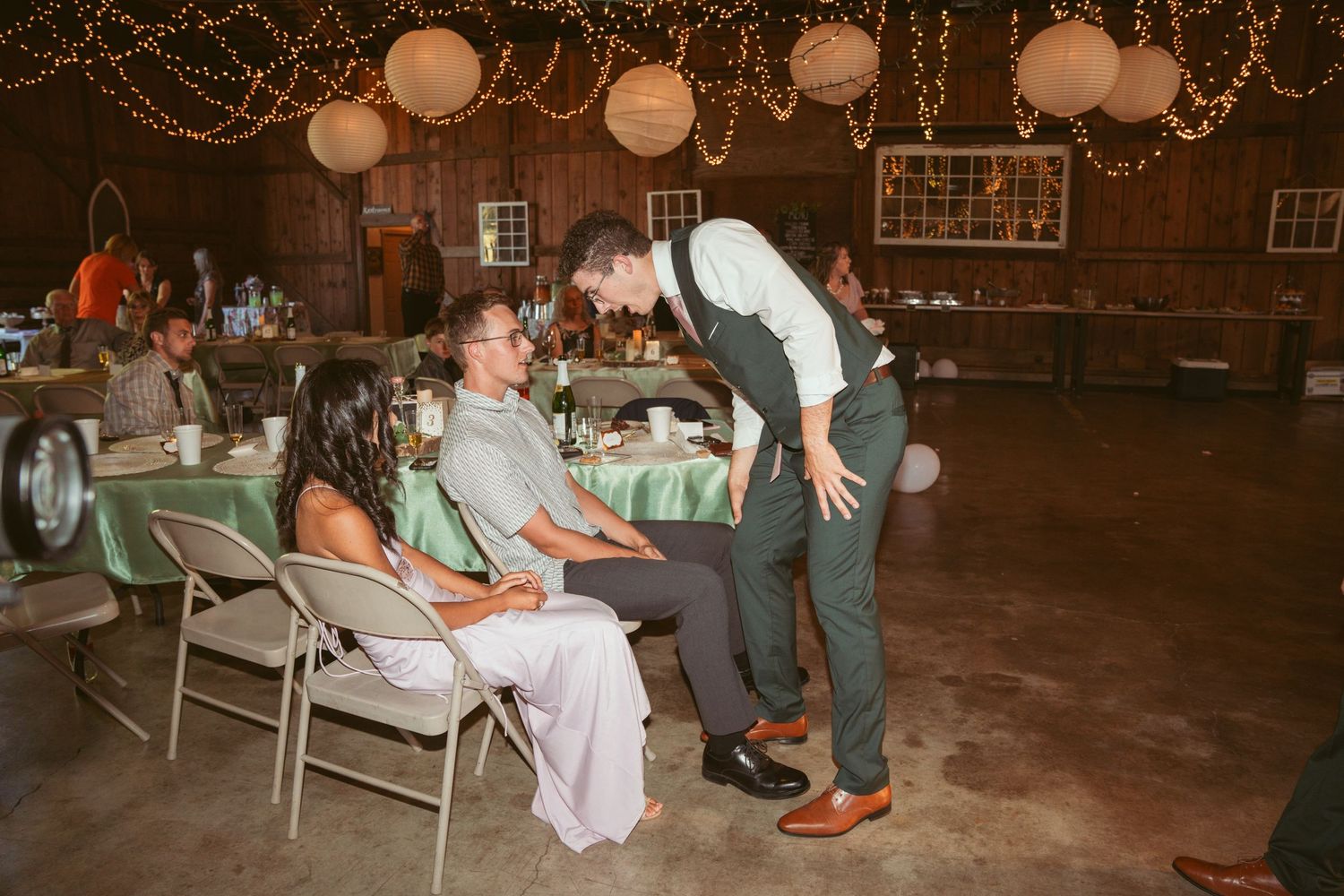 Reception guests seated at tables beside a lively dance floor decorated with string lights.