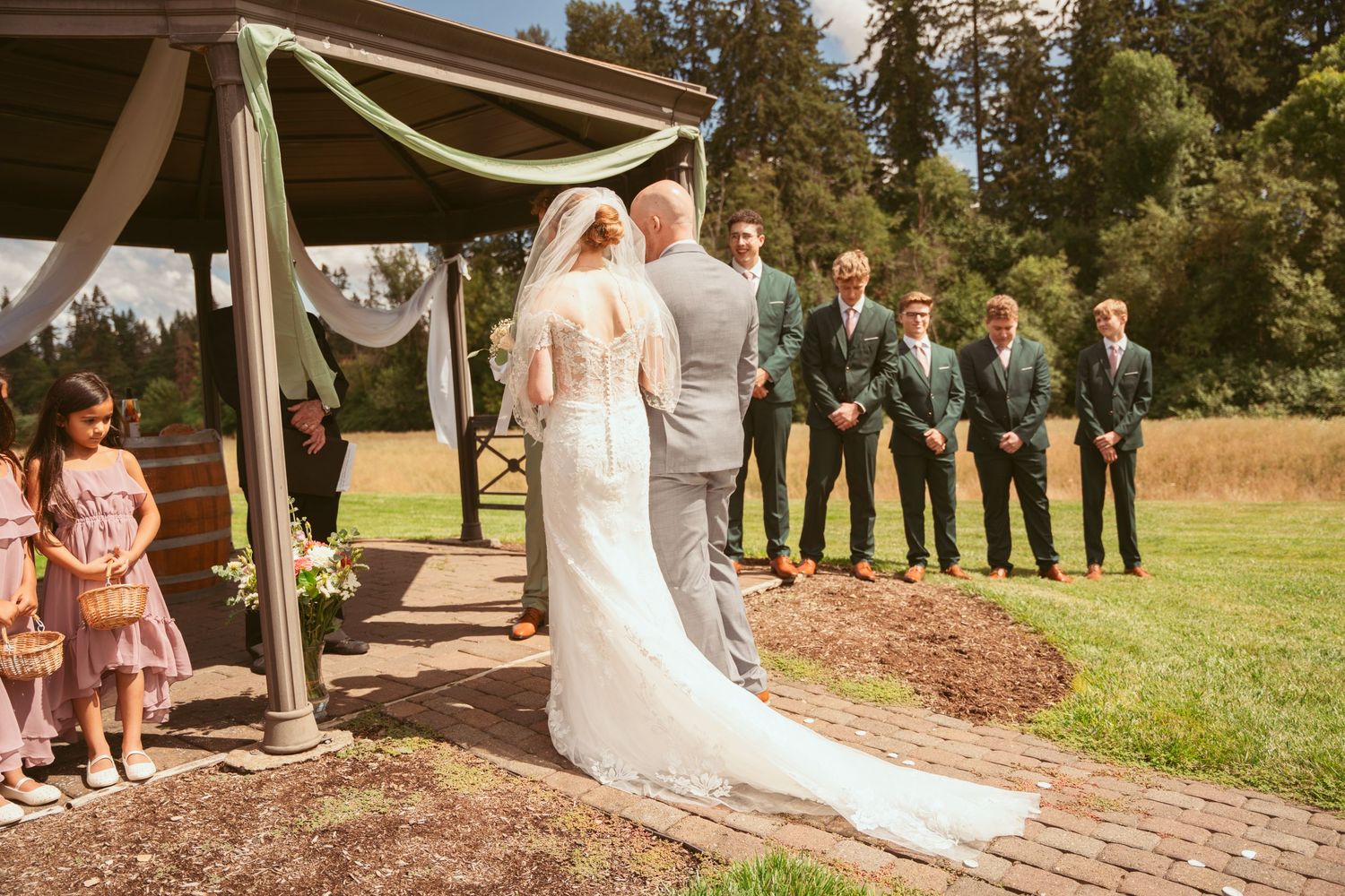 Wedding ceremony processional on a brick pathway with attendants in pink and green attire.
