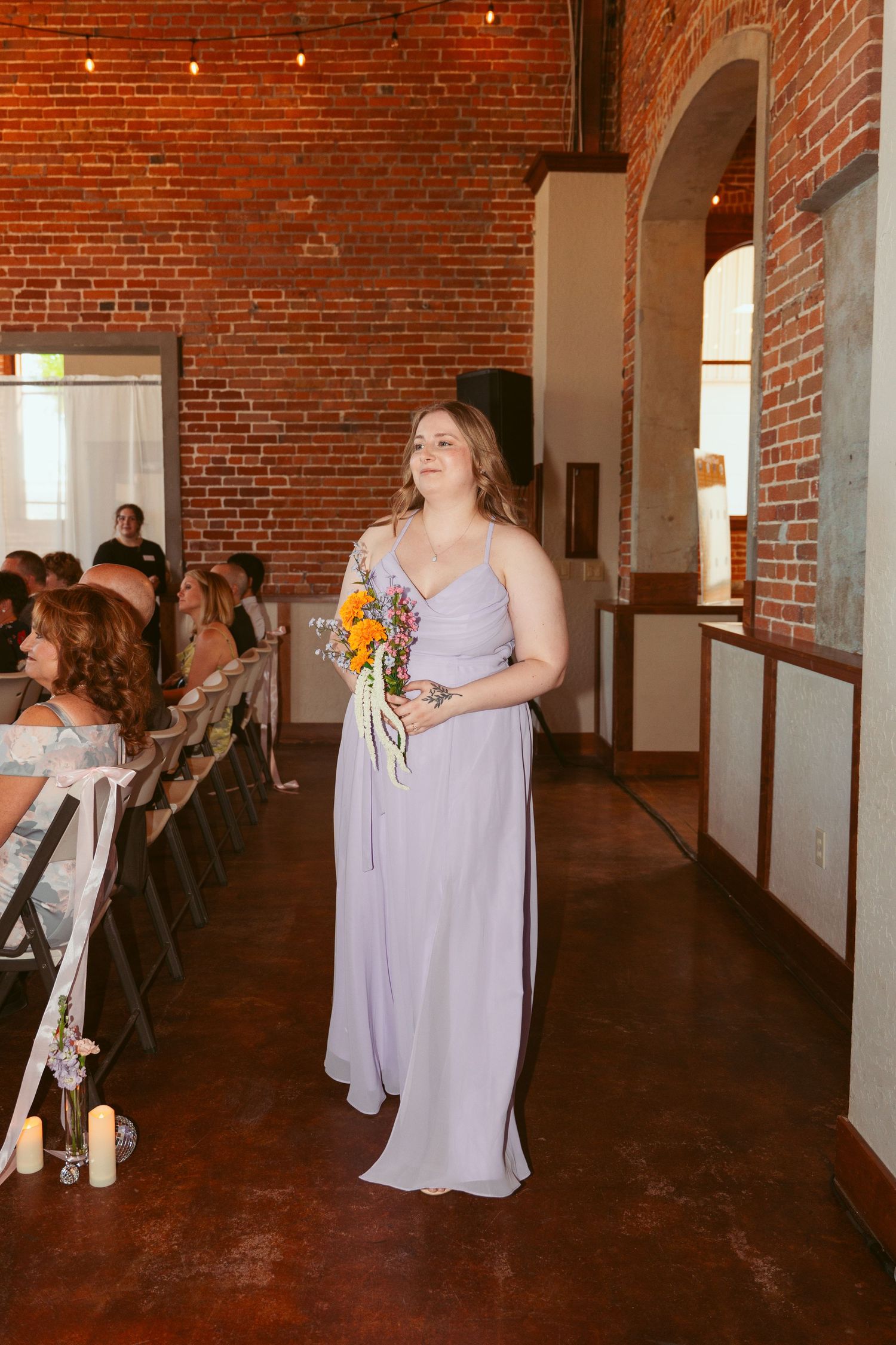 Wedding guests dance and celebrate in a rustic brick-walled venue with string lights overhead.