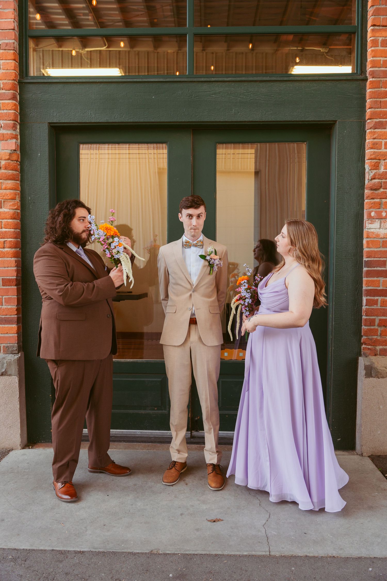 Wedding party members pose in alternating positions wearing brown suits and purple dresses.