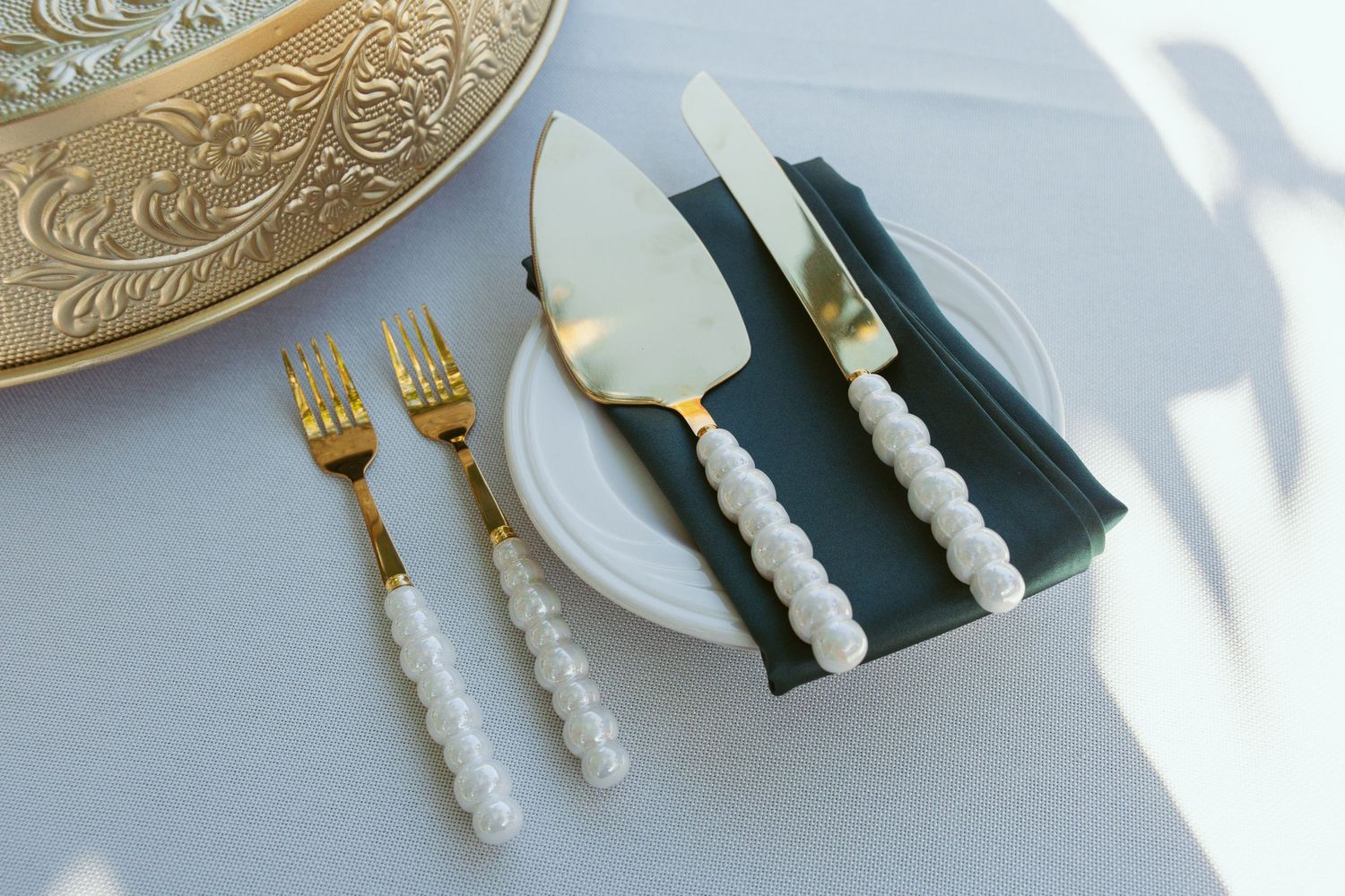 Ornate gold utensils with white handles arranged on a reflective surface.