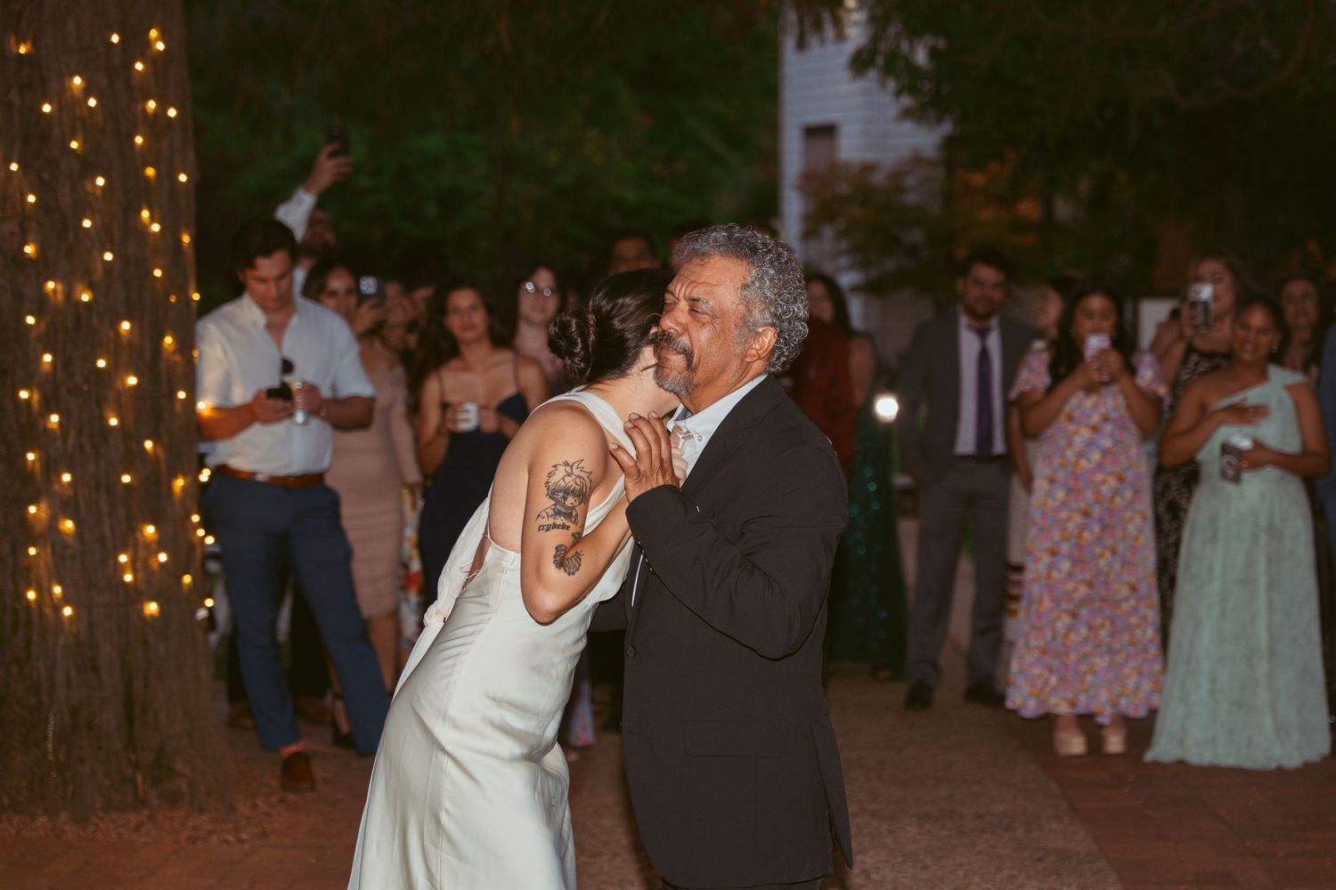 A couple dances together at an outdoor evening wedding reception with guests watching.