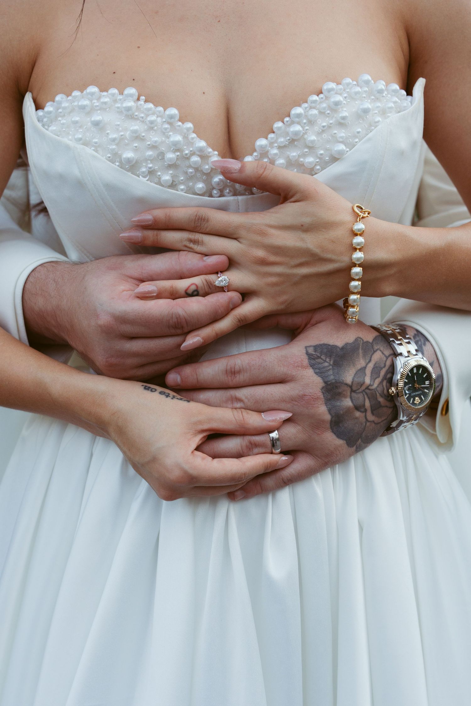 Close-up detail shots of hands wearing wedding rings and jewelry against a white dress.
