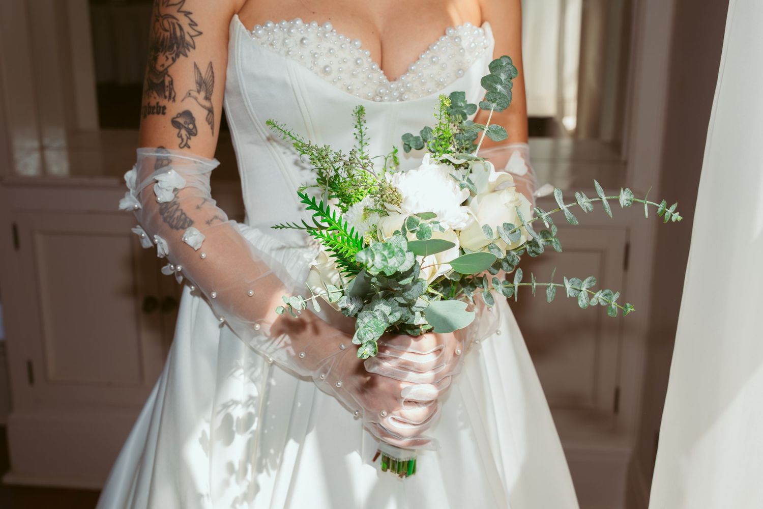 A white wedding dress with delicate lace details and a beautiful bouquet of eucalyptus and greenery.