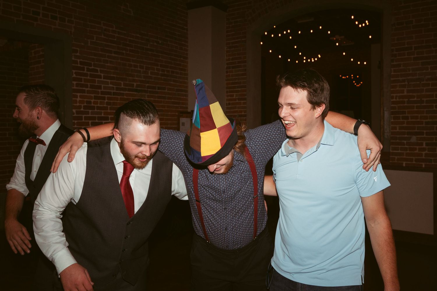 Party guests dancing and socializing under string lights in a brick-walled venue.