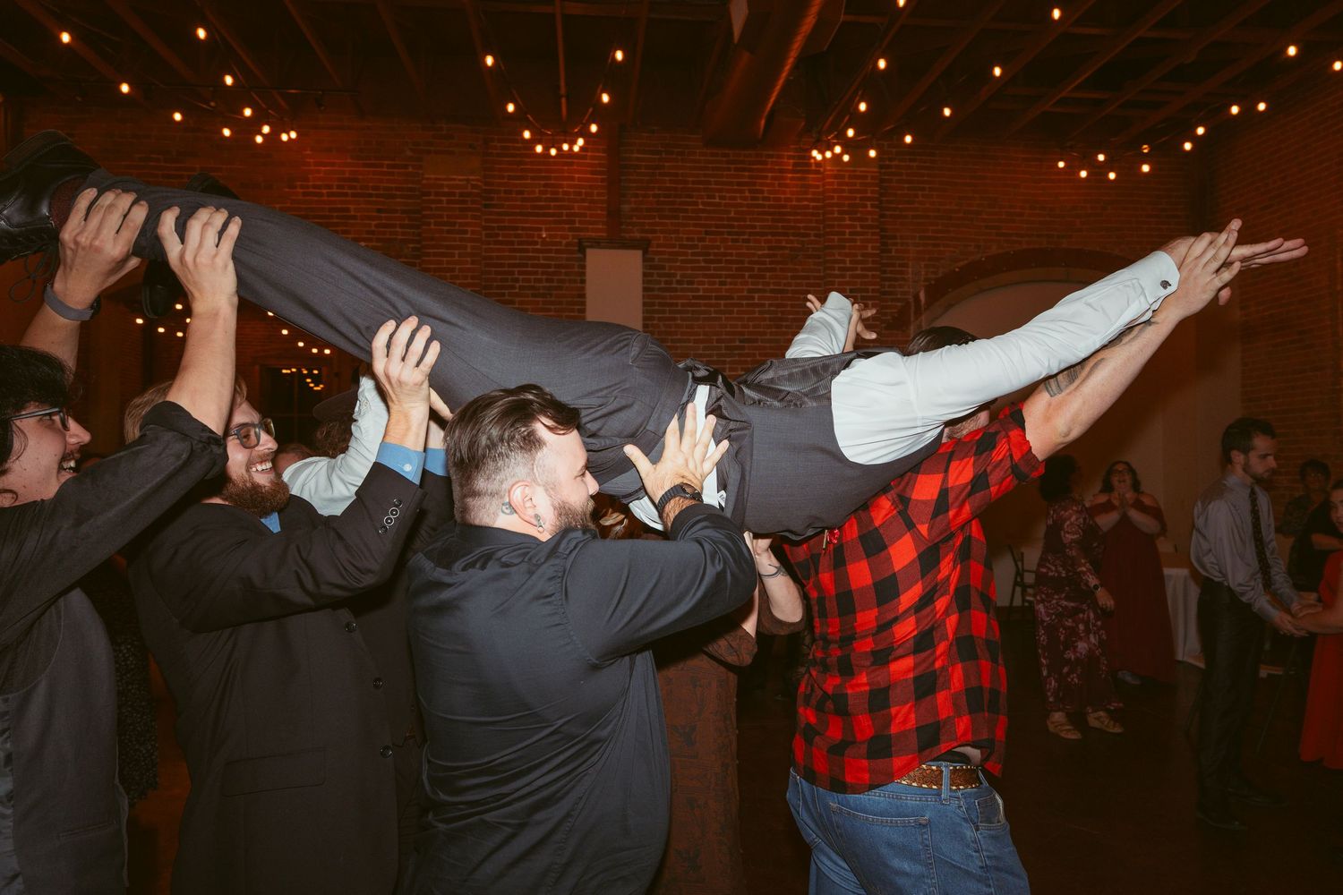 Party guests lifting and supporting someone horizontally during an energetic dance celebration.