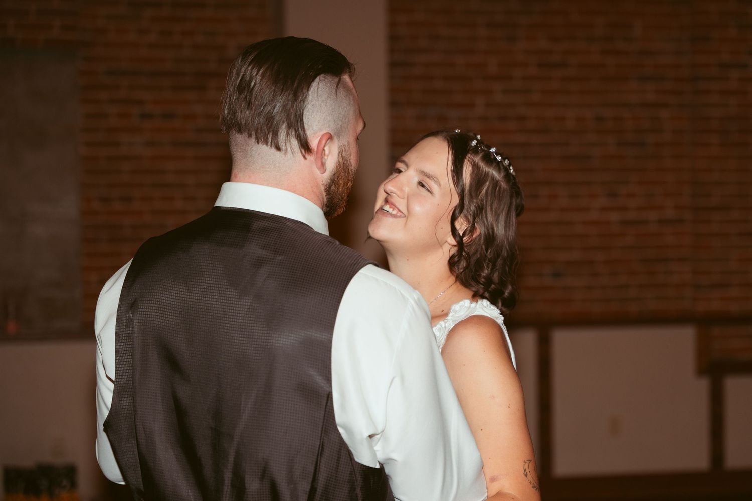 A candid moment of joy shared between newlyweds against a brick wall background.