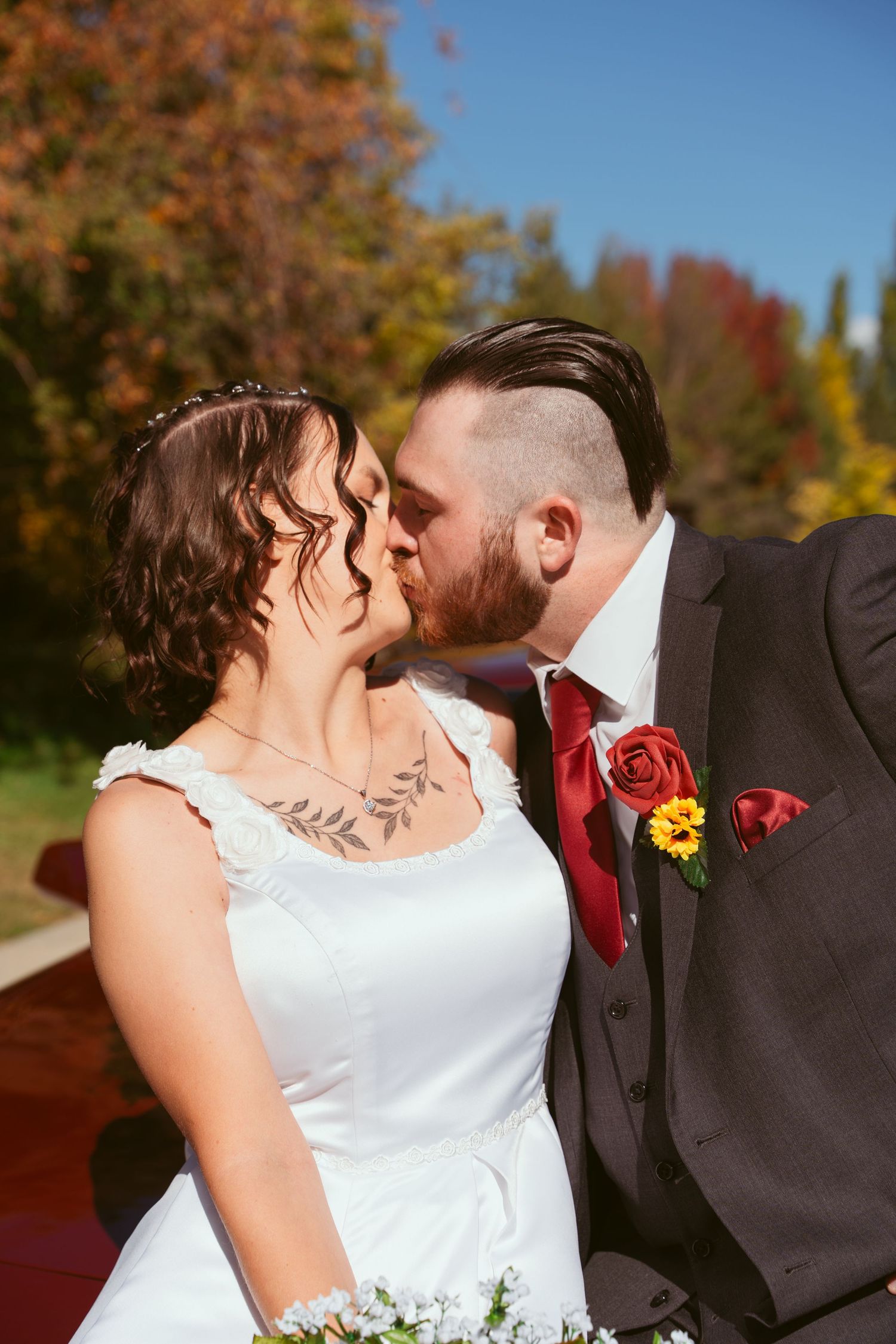 Romantic wedding portrait with couple sharing kiss against autumn backdrop.