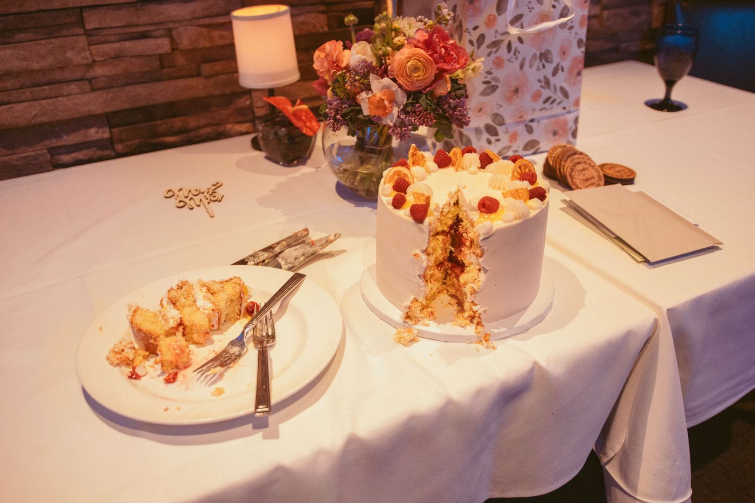 Wedding cake and desserts displayed on white tablecloth with floral decorations.
