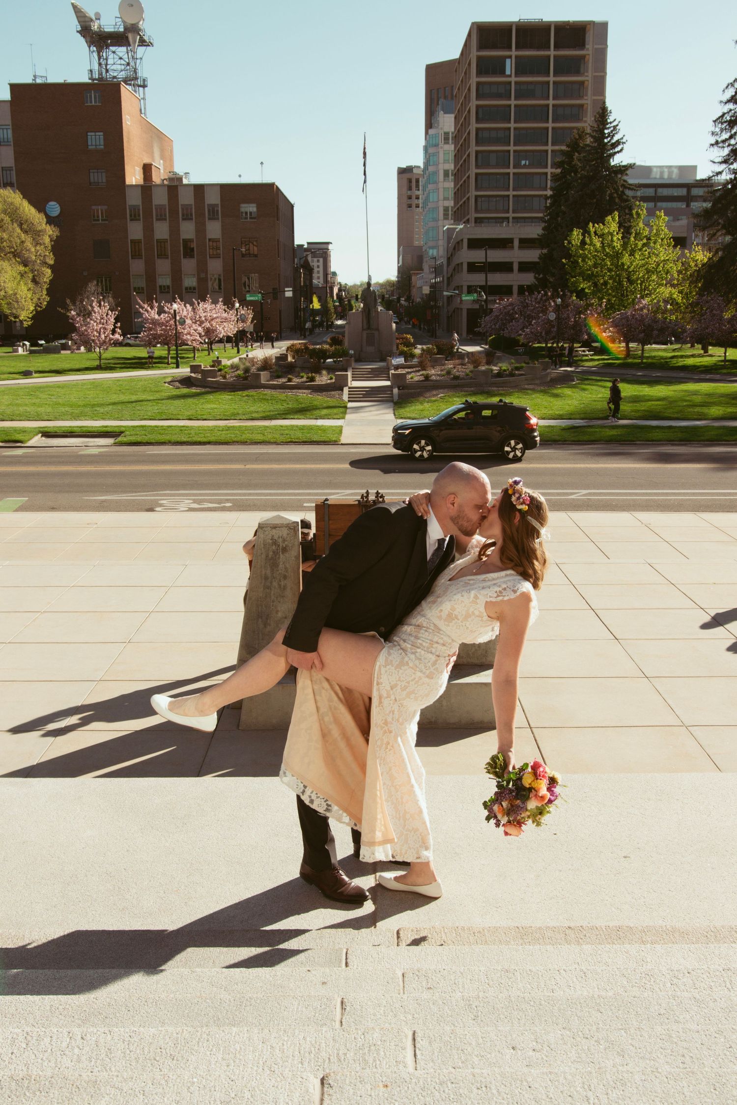 A dramatic dip kiss between newlyweds on an urban sidewalk with city buildings in the background.