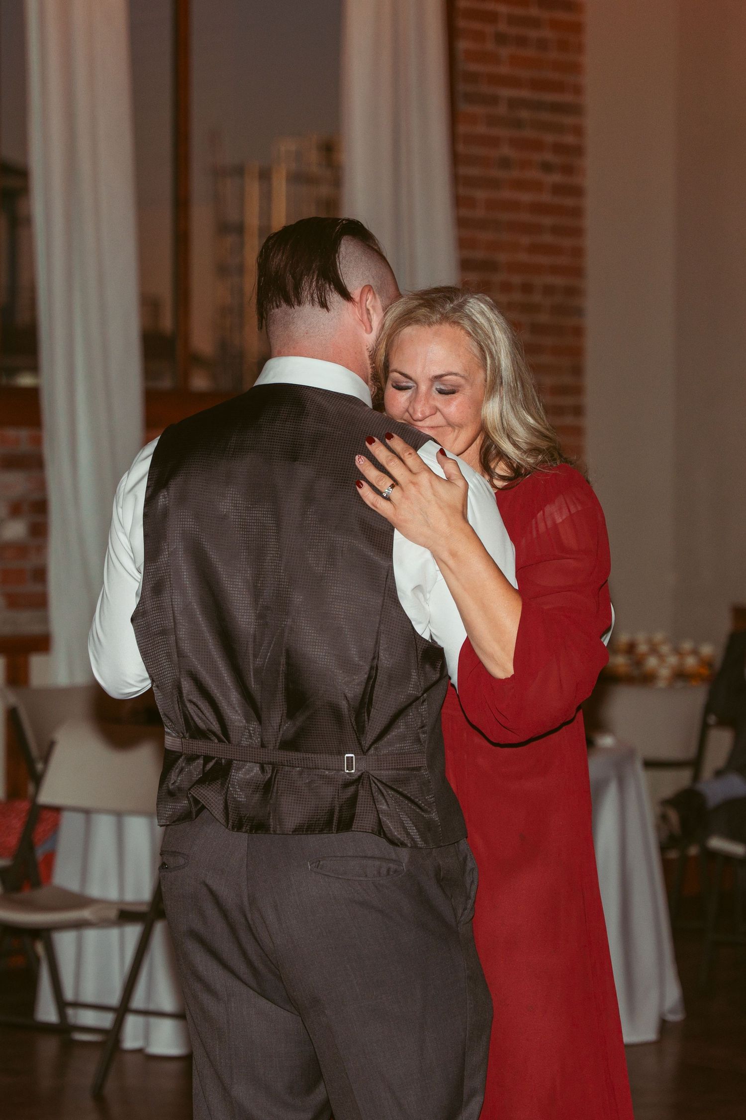 Dancers performing an intimate slow dance in a reception hall with exposed brick walls.