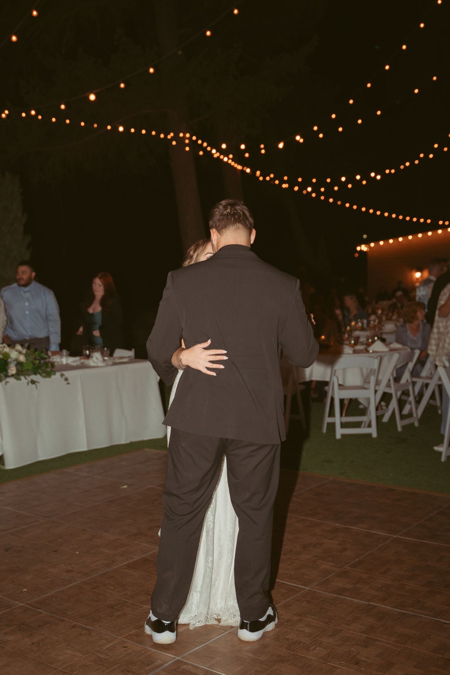 Wedding guests dancing together on a dark dance floor under romantic string lights.