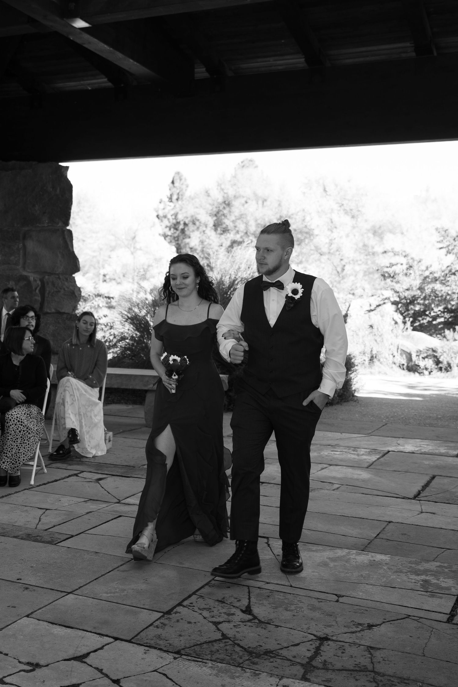 Black and white image showing people standing on a stone patio during an event.