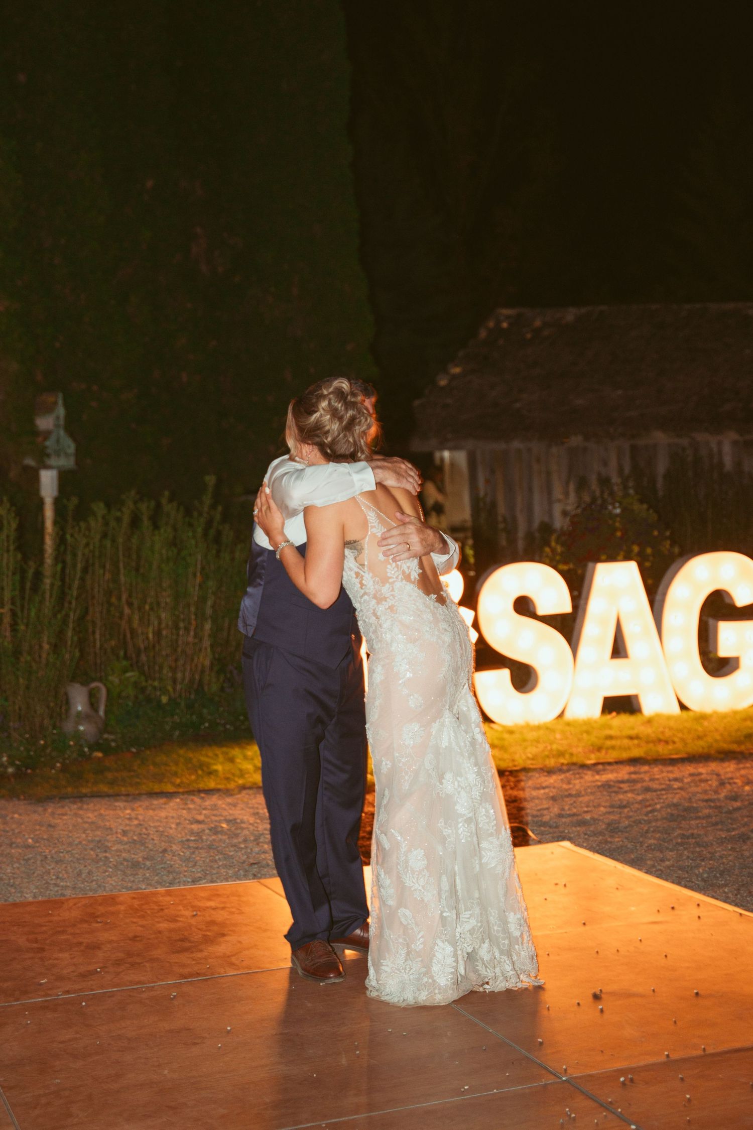 A couple embraces on the dance floor with illuminated SAGE sign in background.
