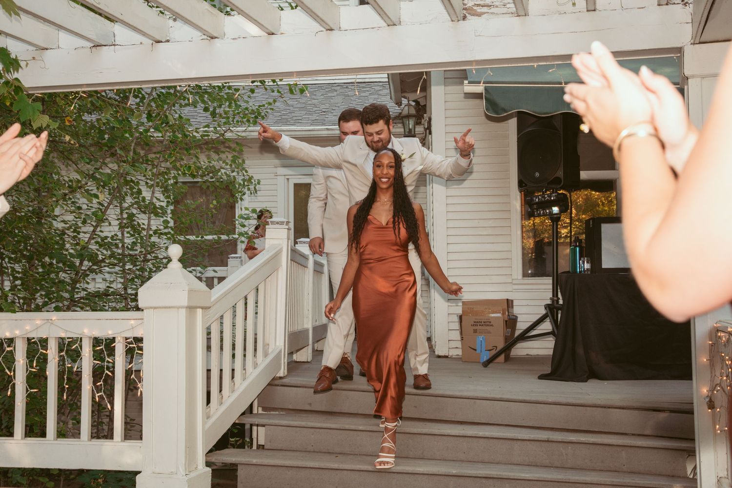 Guests in formal attire dance and celebrate under a white pergola at an outdoor wedding reception.