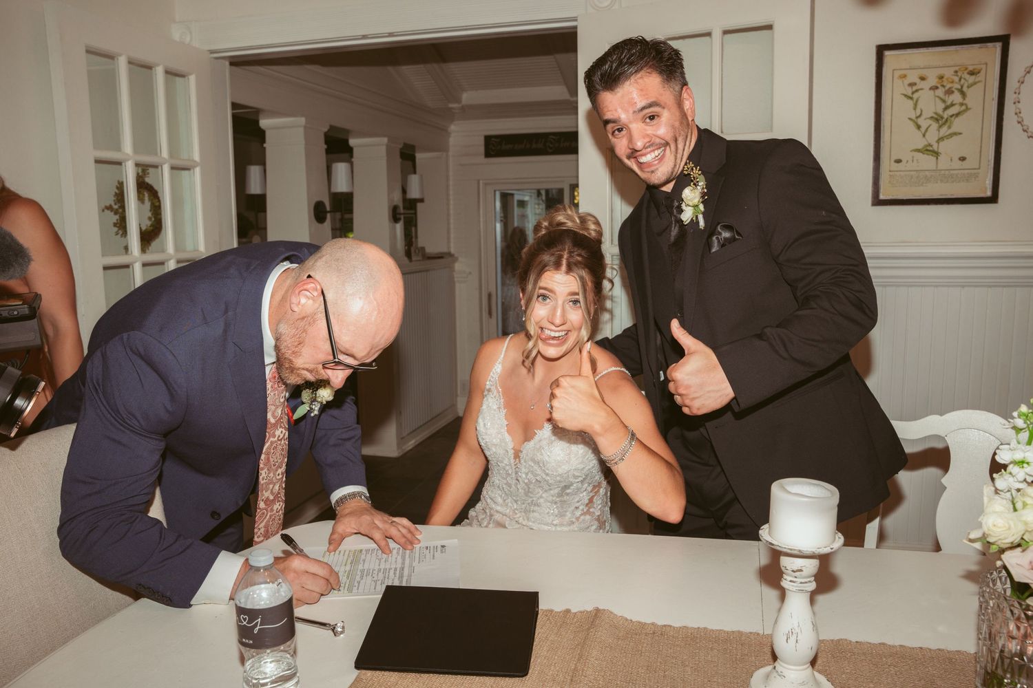 Wedding party members sharing drinks and laughs during indoor reception celebrations.