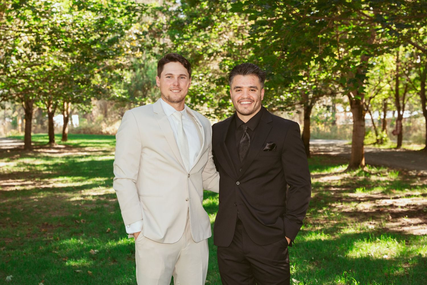 Two people in contrasting light and dark suits share a candid moment outdoors.