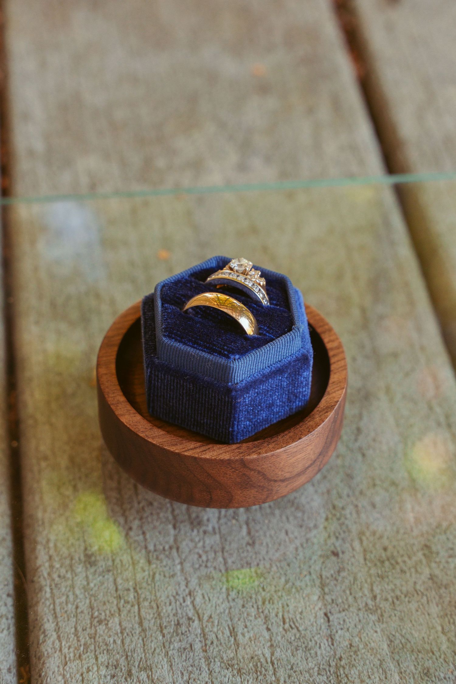 Engagement ring nestled in a navy blue velvet ring box on wooden surface.