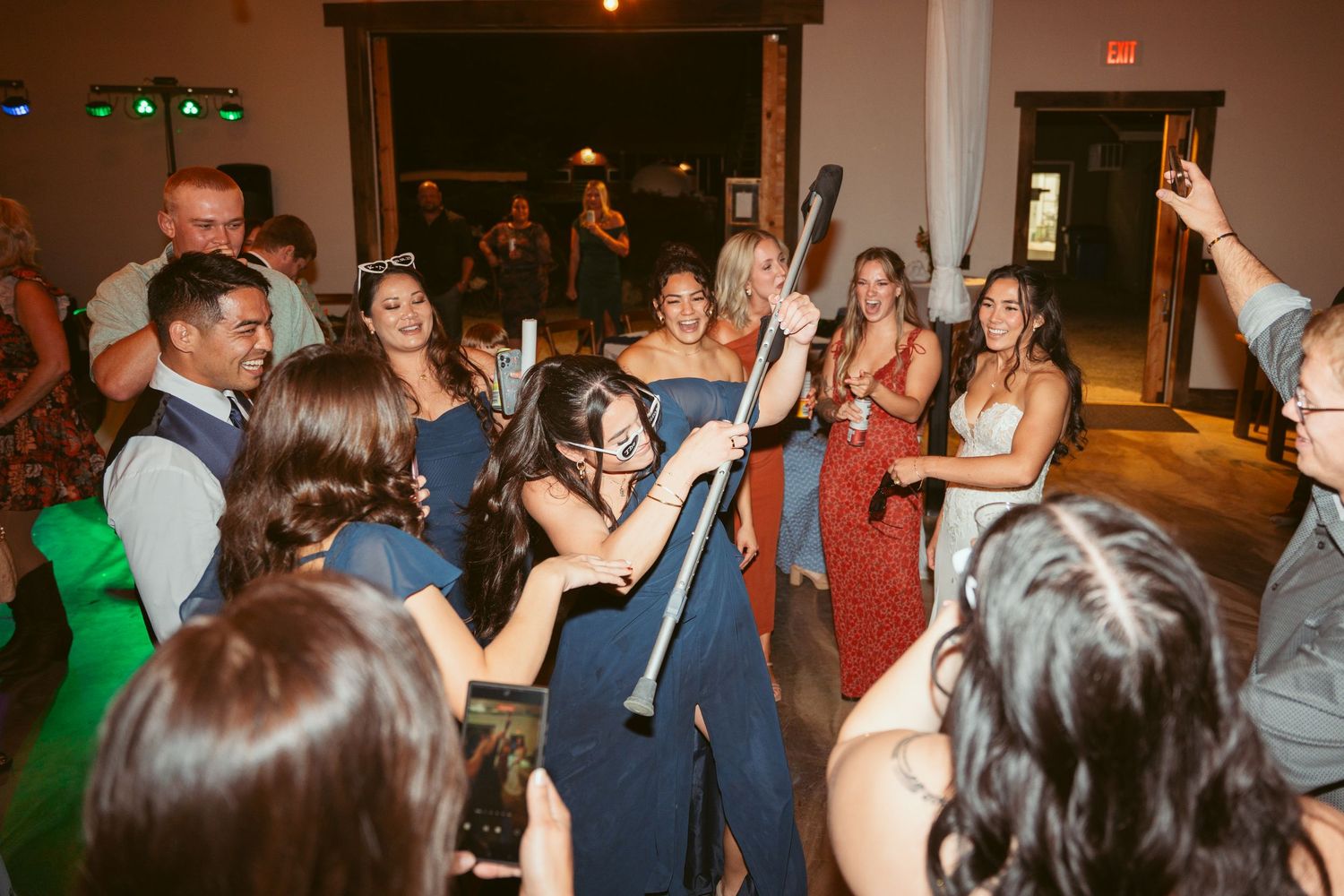 Party guests hold up glow sticks while dancing energetically at a wedding reception.