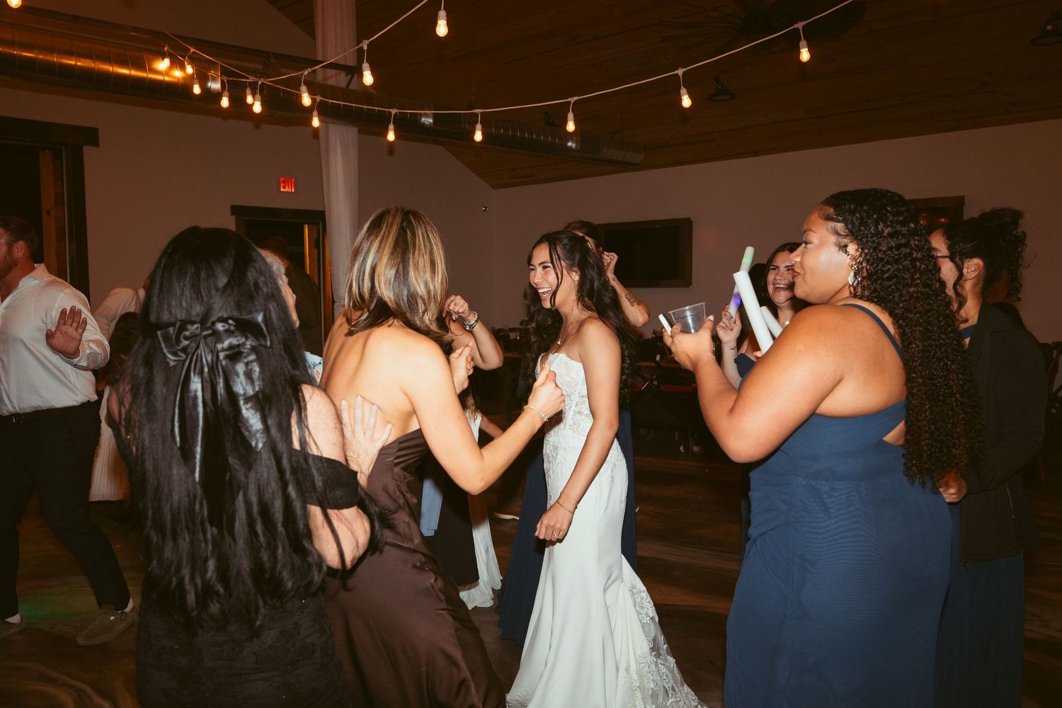 Crowd dancing and celebrating at an indoor event with string lights decorating the ceiling.