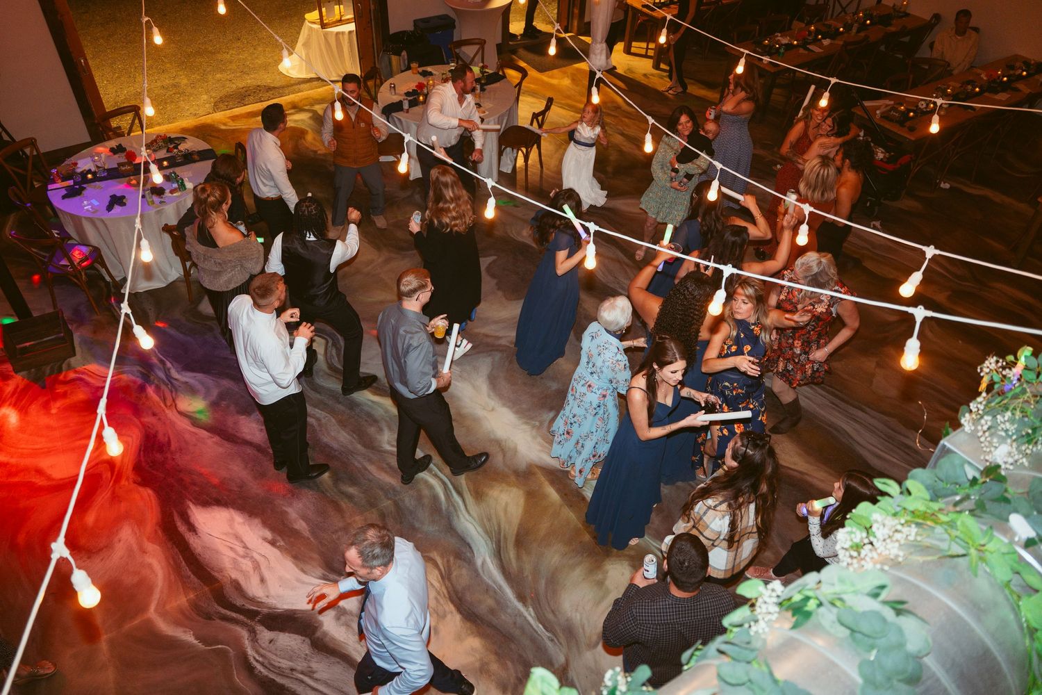 Wedding guests dancing and celebrating under warm string lights at indoor reception.