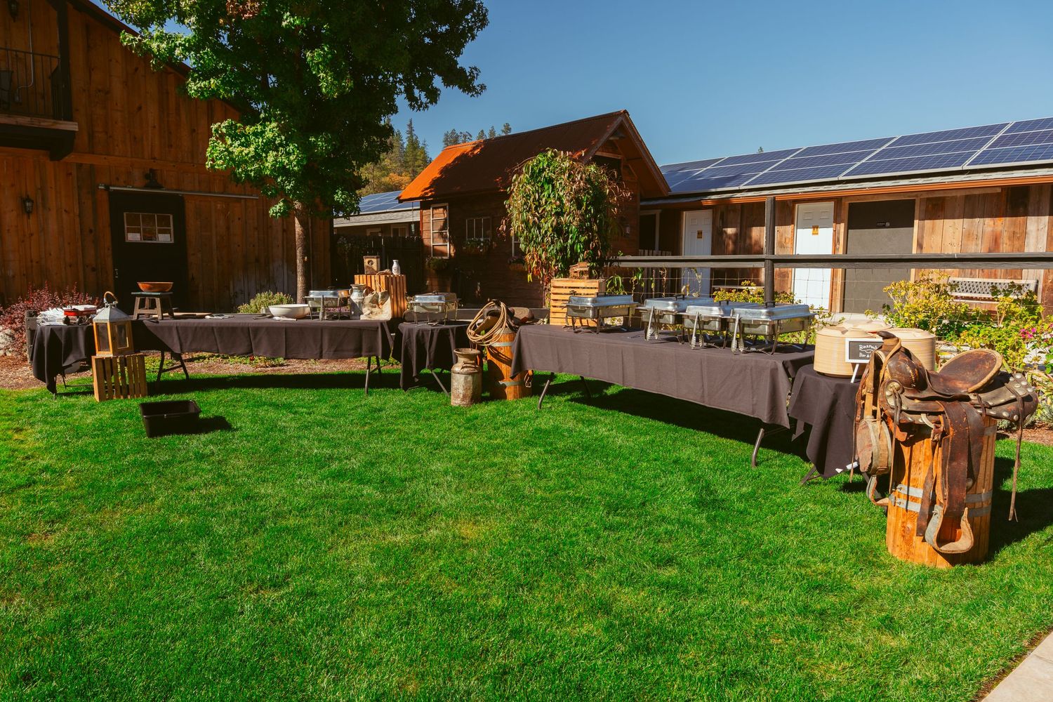 Rustic outdoor wedding venue with wooden barn and solar panels visible in sunlight.