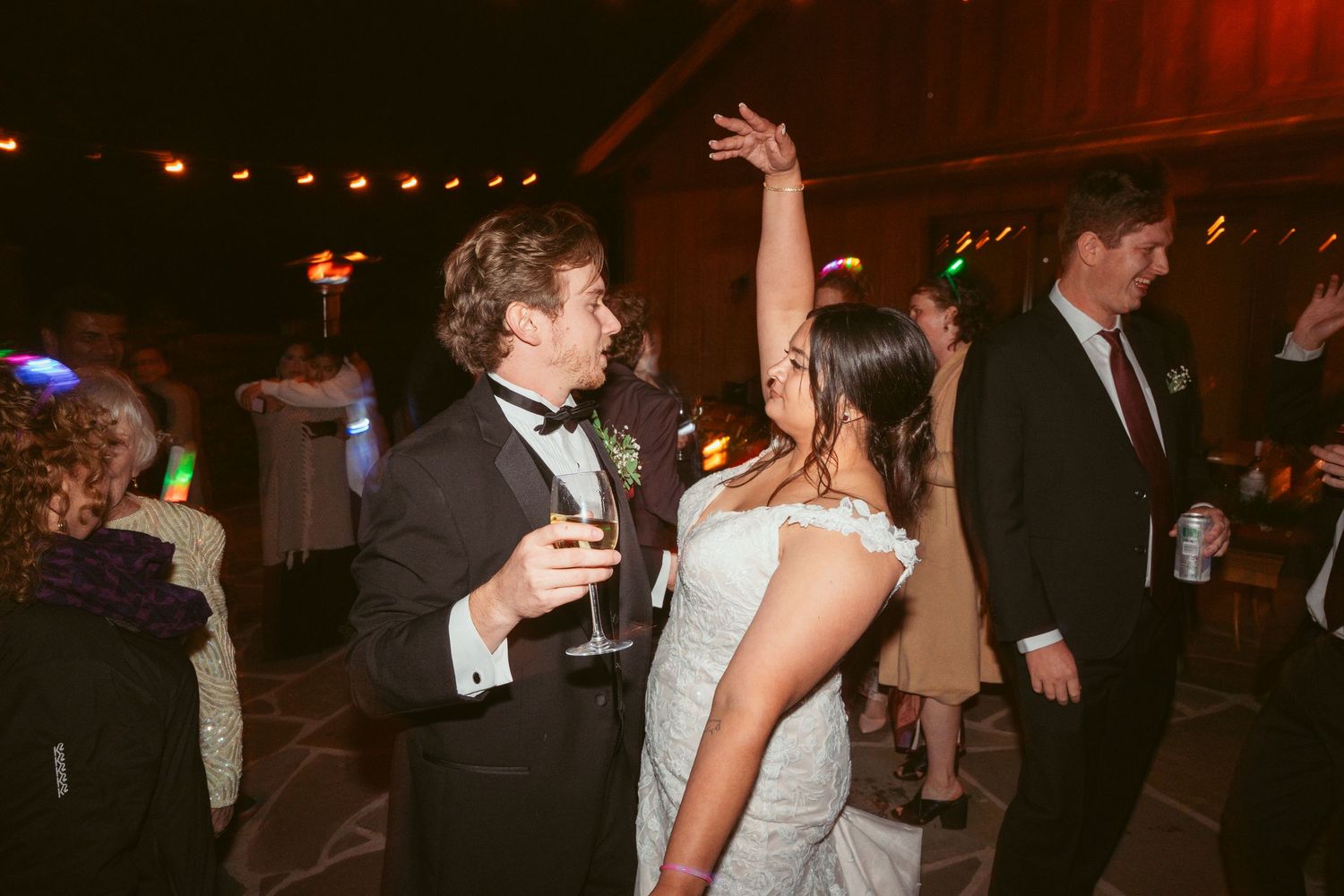 Wedding guests dancing and mingling under decorative string lights at night.