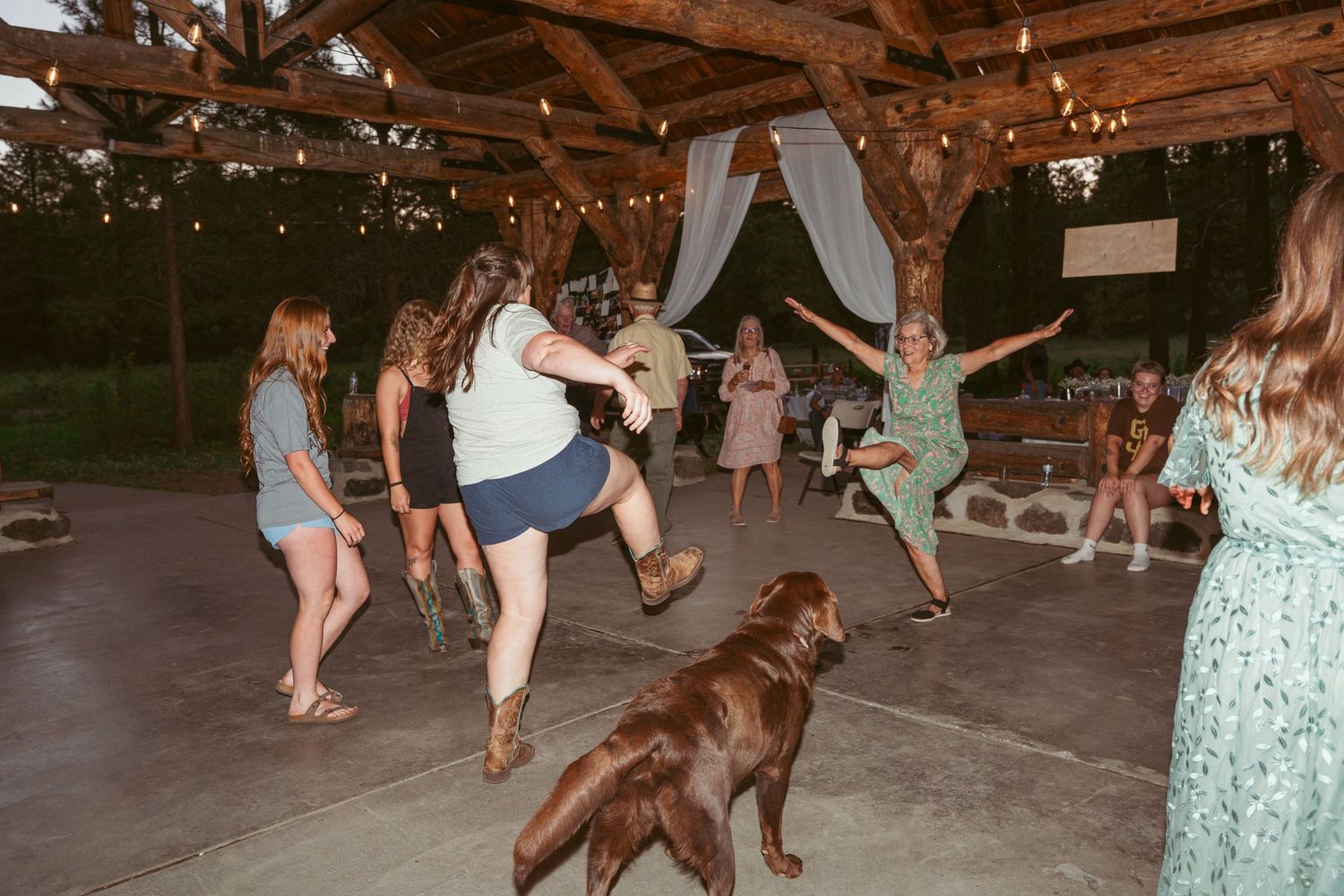 Guests perform a synchronized dance routine at a rustic outdoor wedding reception.