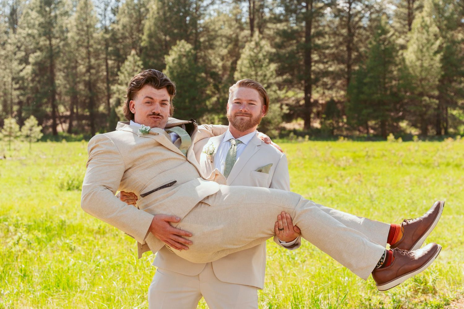 Wedding party members in light suits perform playful lifts and poses outdoors.