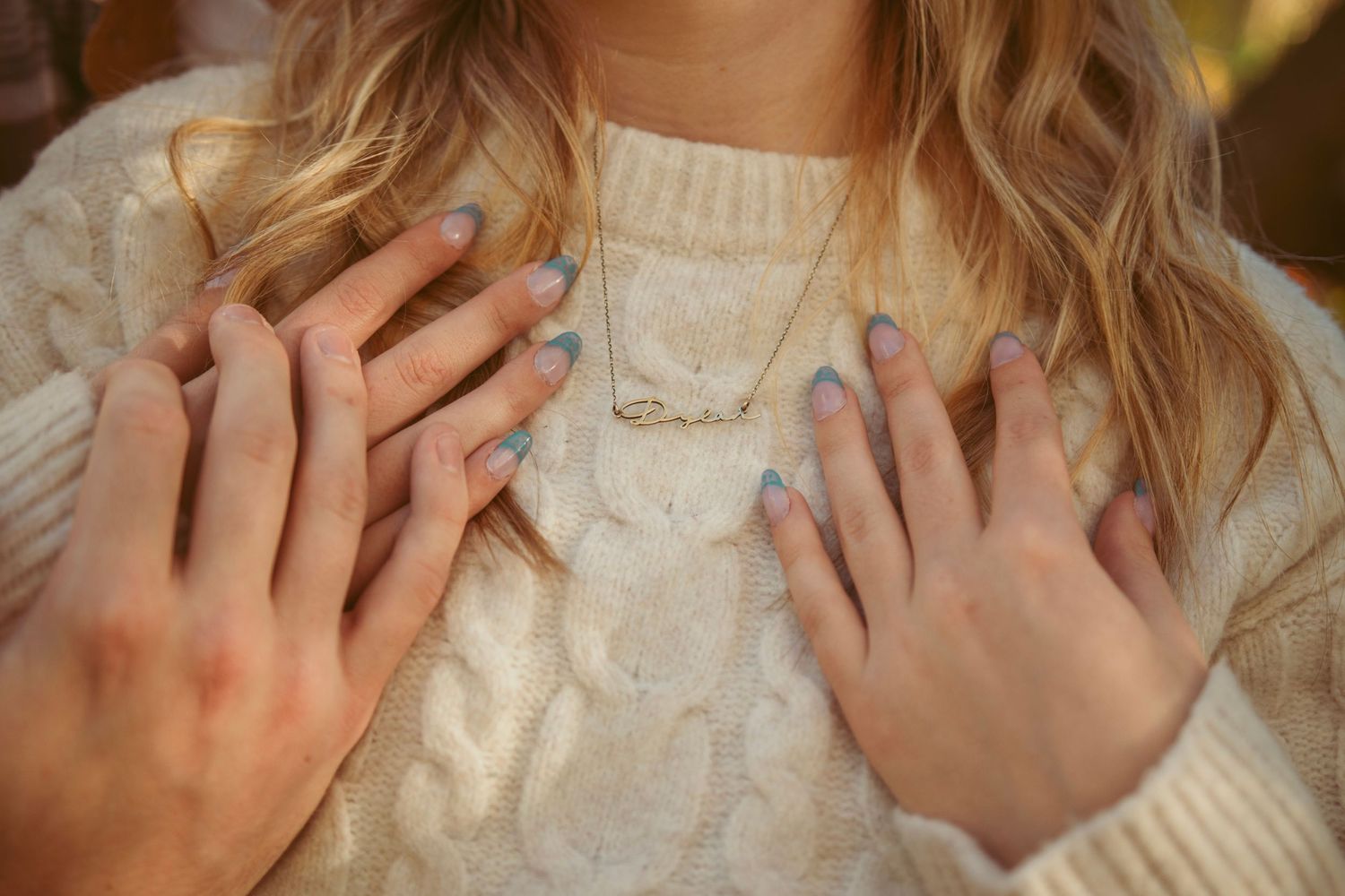 Close-up of hands against cream sweater in natural lighting.
