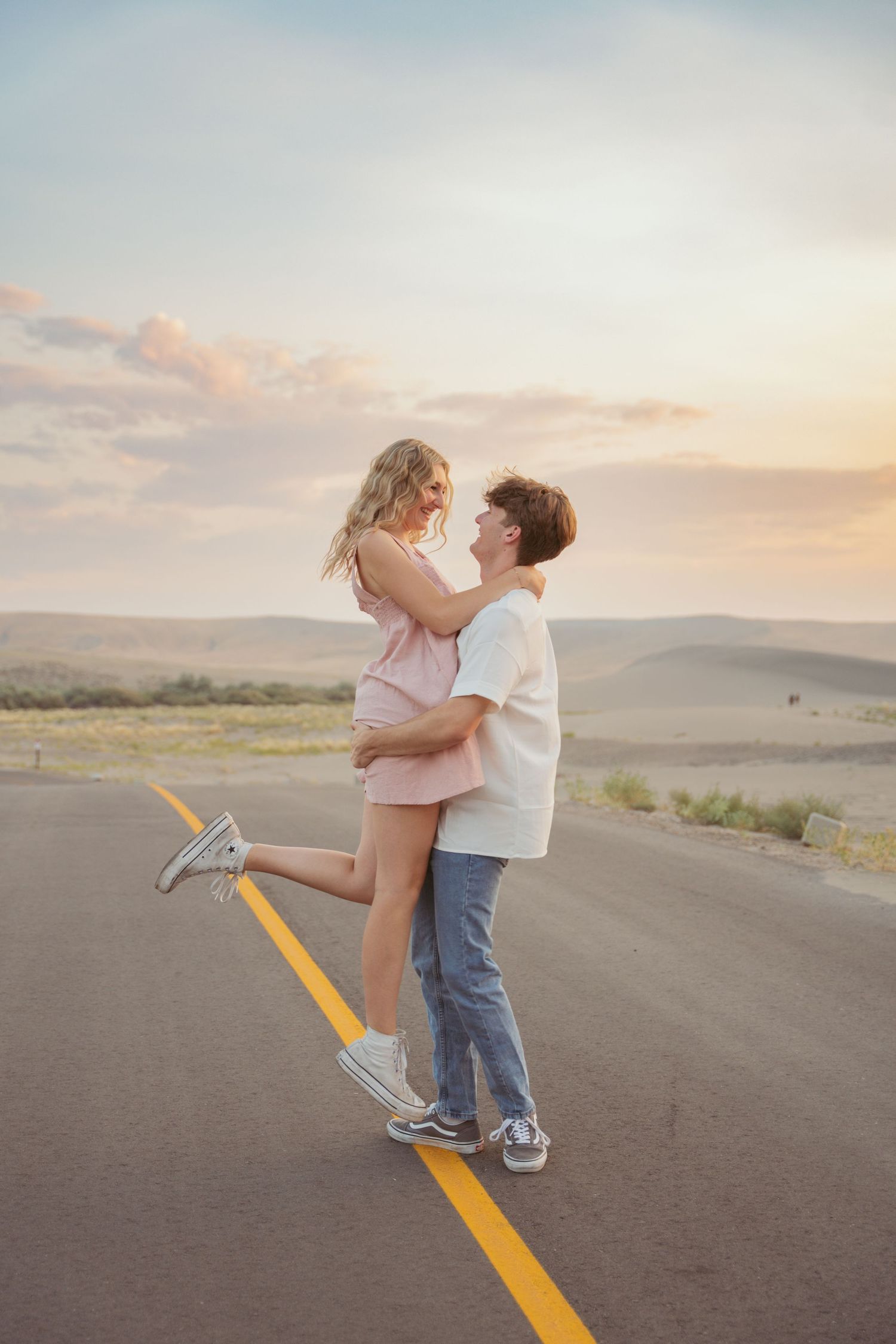 Couple shares a tender moment while standing on a yellow line in the middle of a desert road.