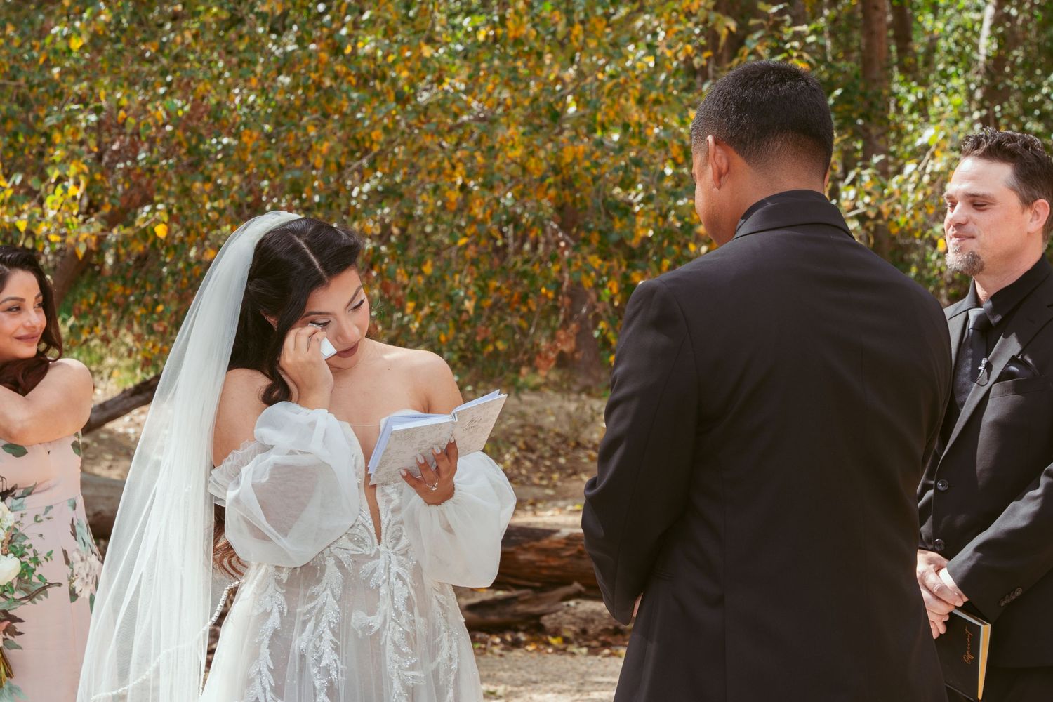 Emotional wedding ceremony moment as bride reads vows outdoors in autumn setting.