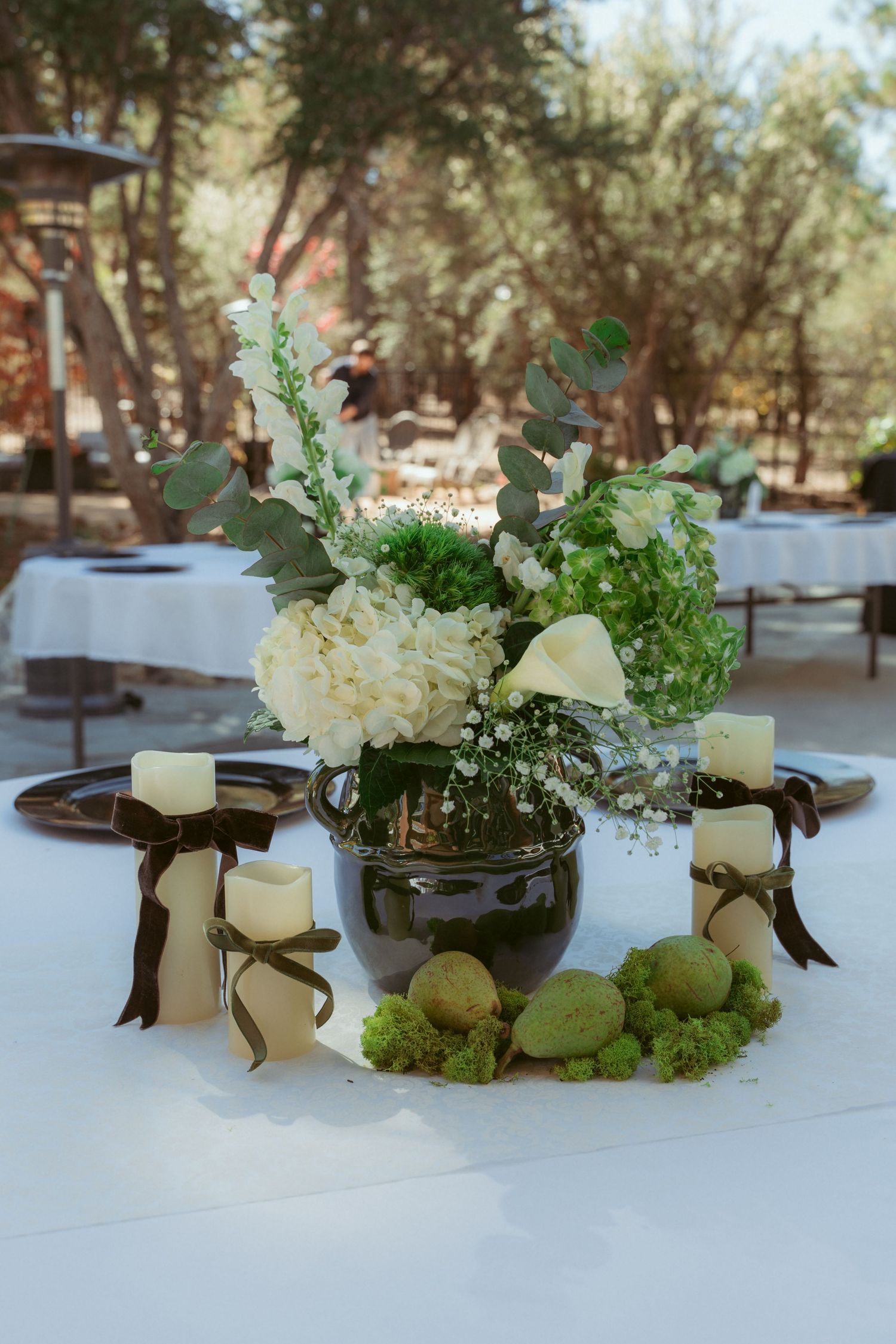 Elegant table centerpieces featuring white candles, flowers and moss on white linens.