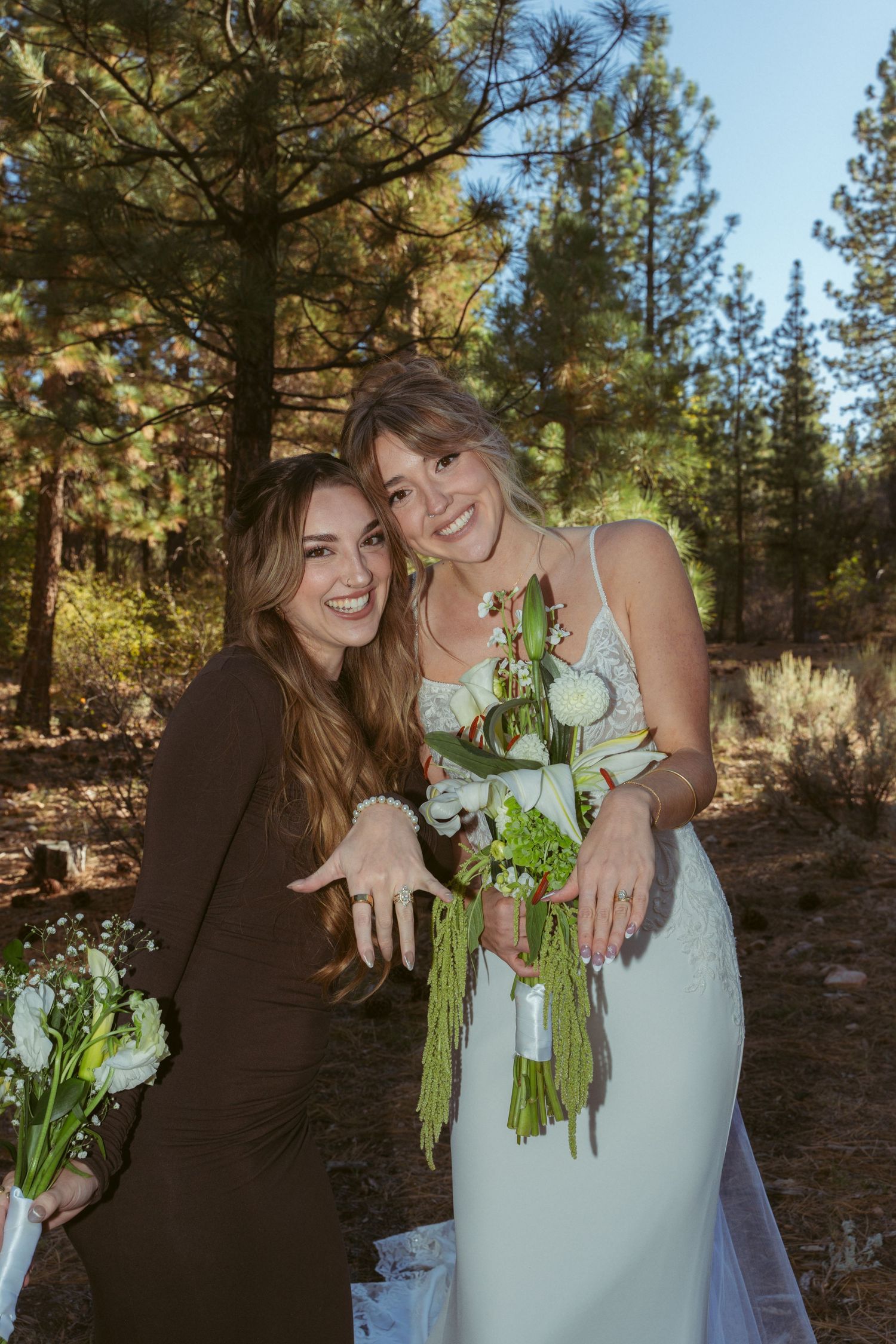 Wedding party members share joyful moment with bouquets in forest setting.