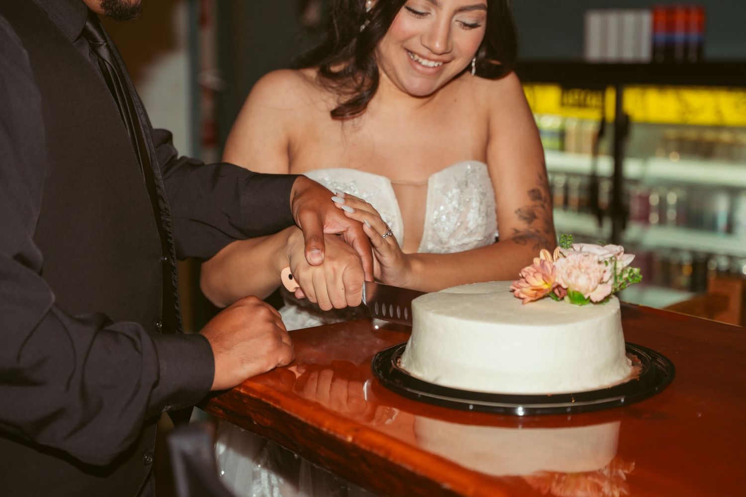 Newlyweds cut into their white wedding cake together during their reception celebration.