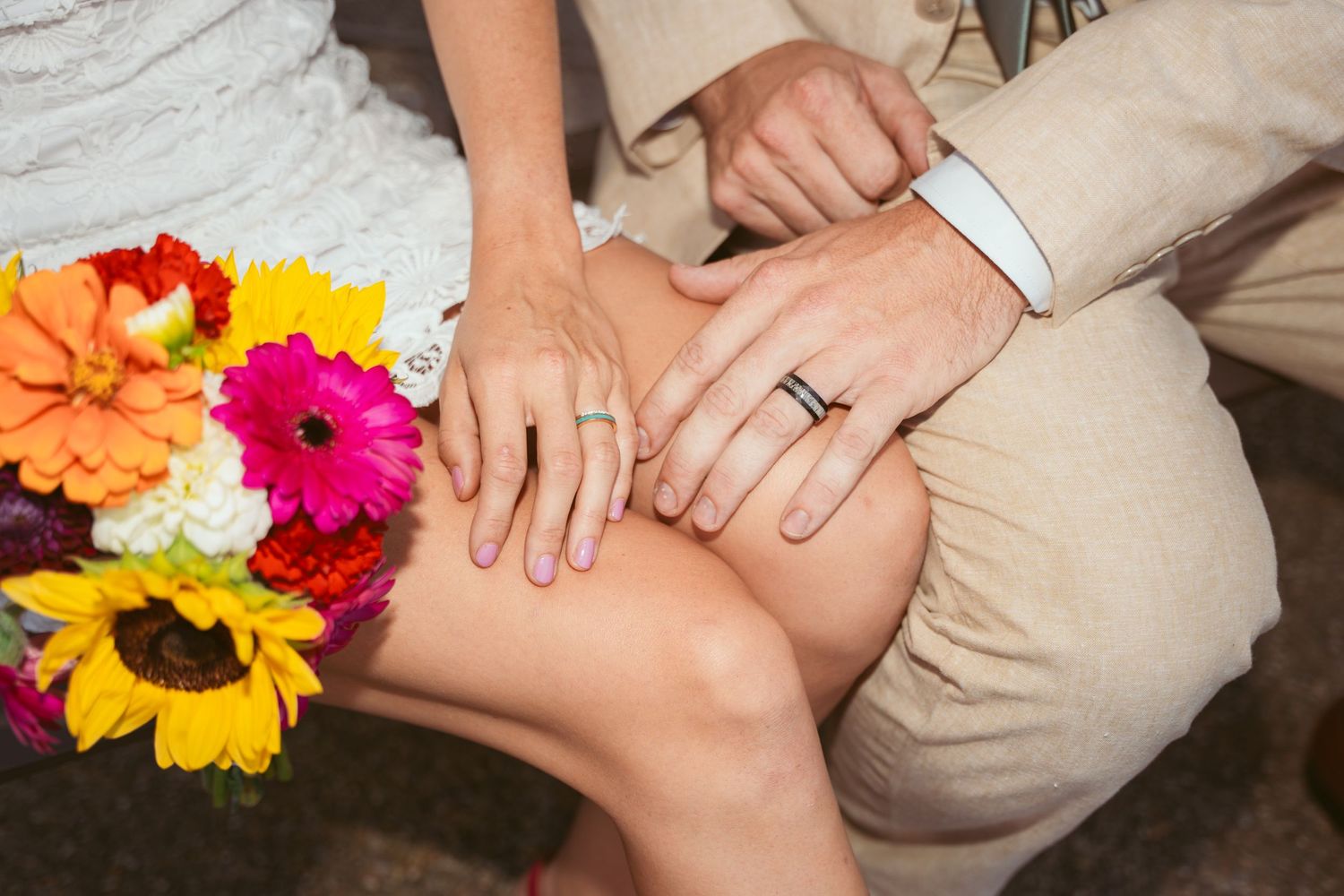 Close up of hands with wedding rings and bright sunflowers in the background.