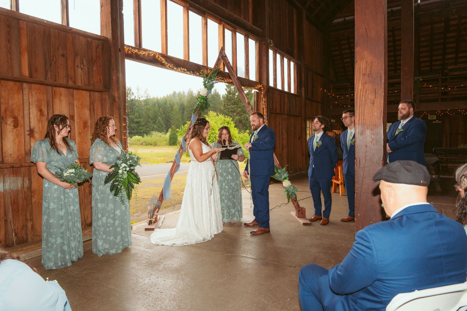 Wide view of rustic barn wedding ceremony with wooden beams and natural lighting.