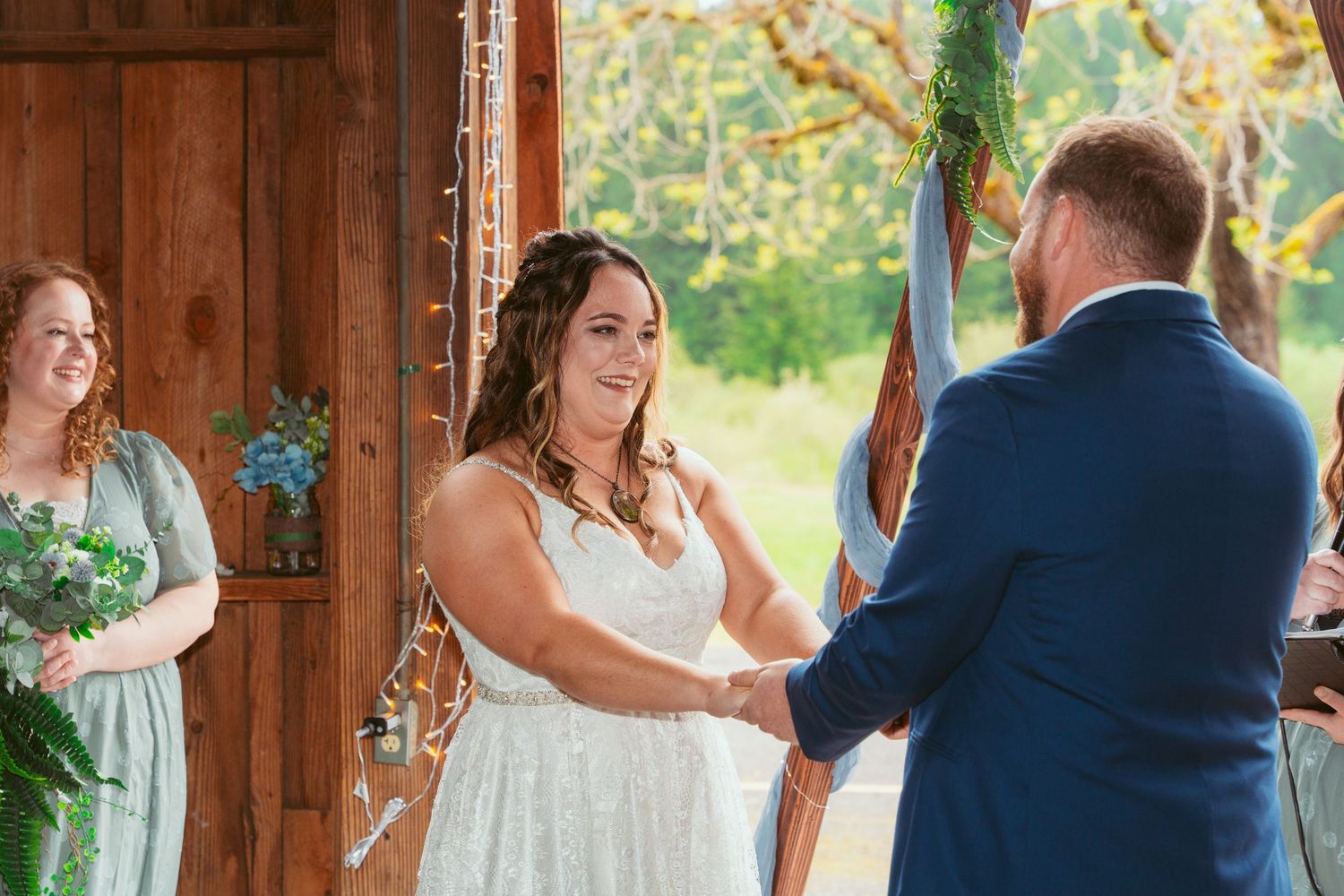 Couple sharing romantic first dance moment in rustic barn with decorative greenery.
