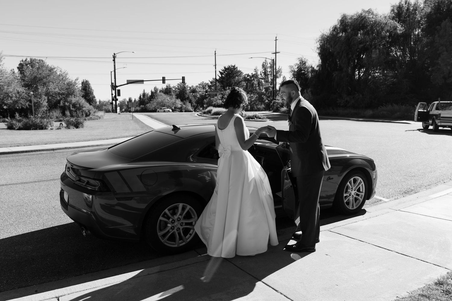 Black and white photo of a couple in formal attire standing beside their car.
