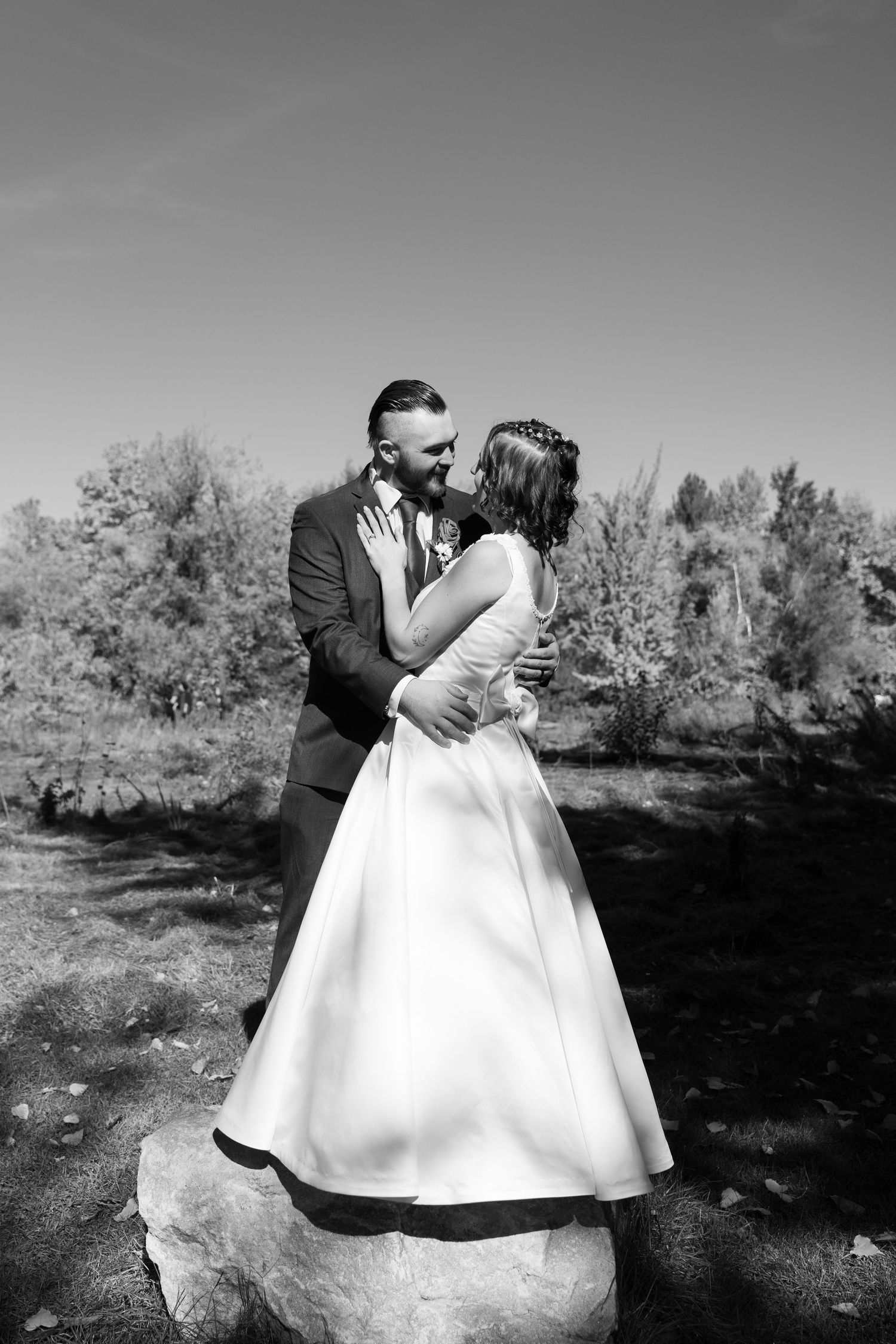A black and white portrait of newlyweds standing on a rock in a natural outdoor setting.
