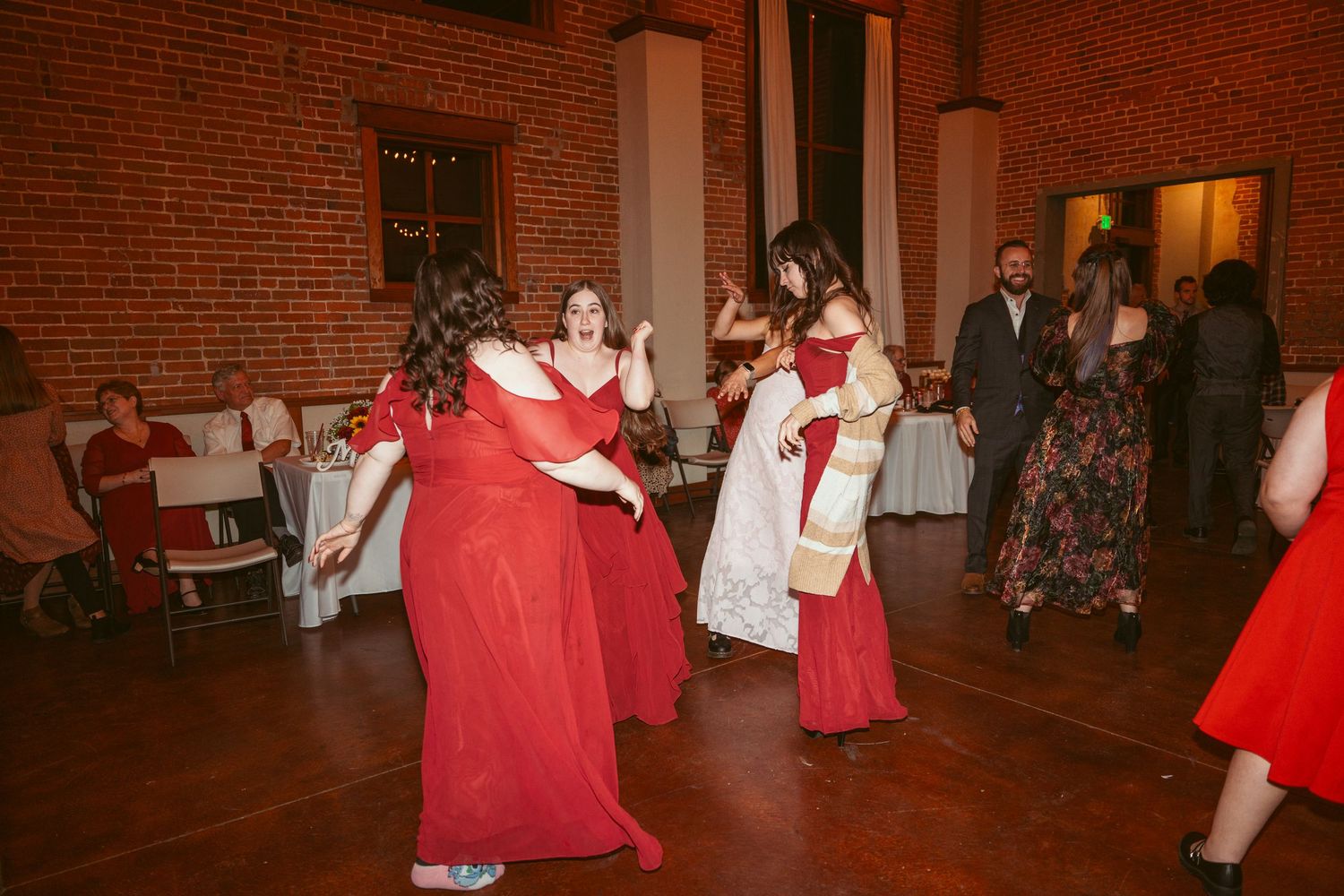 Wedding guests dancing and celebrating in a rustic brick venue with warm lighting.