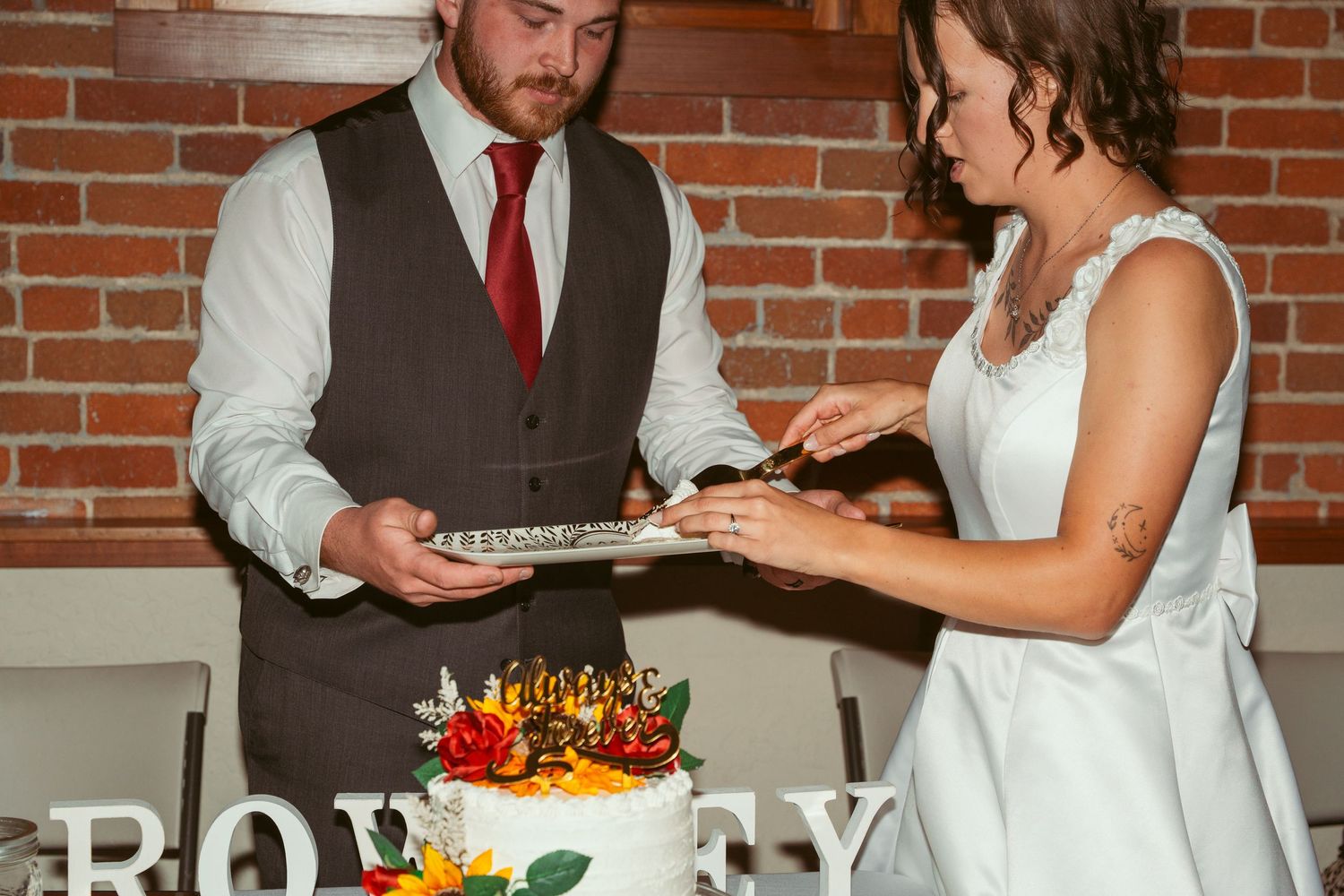Wedding reception scene with cake cutting and dancing in a brick-walled venue.