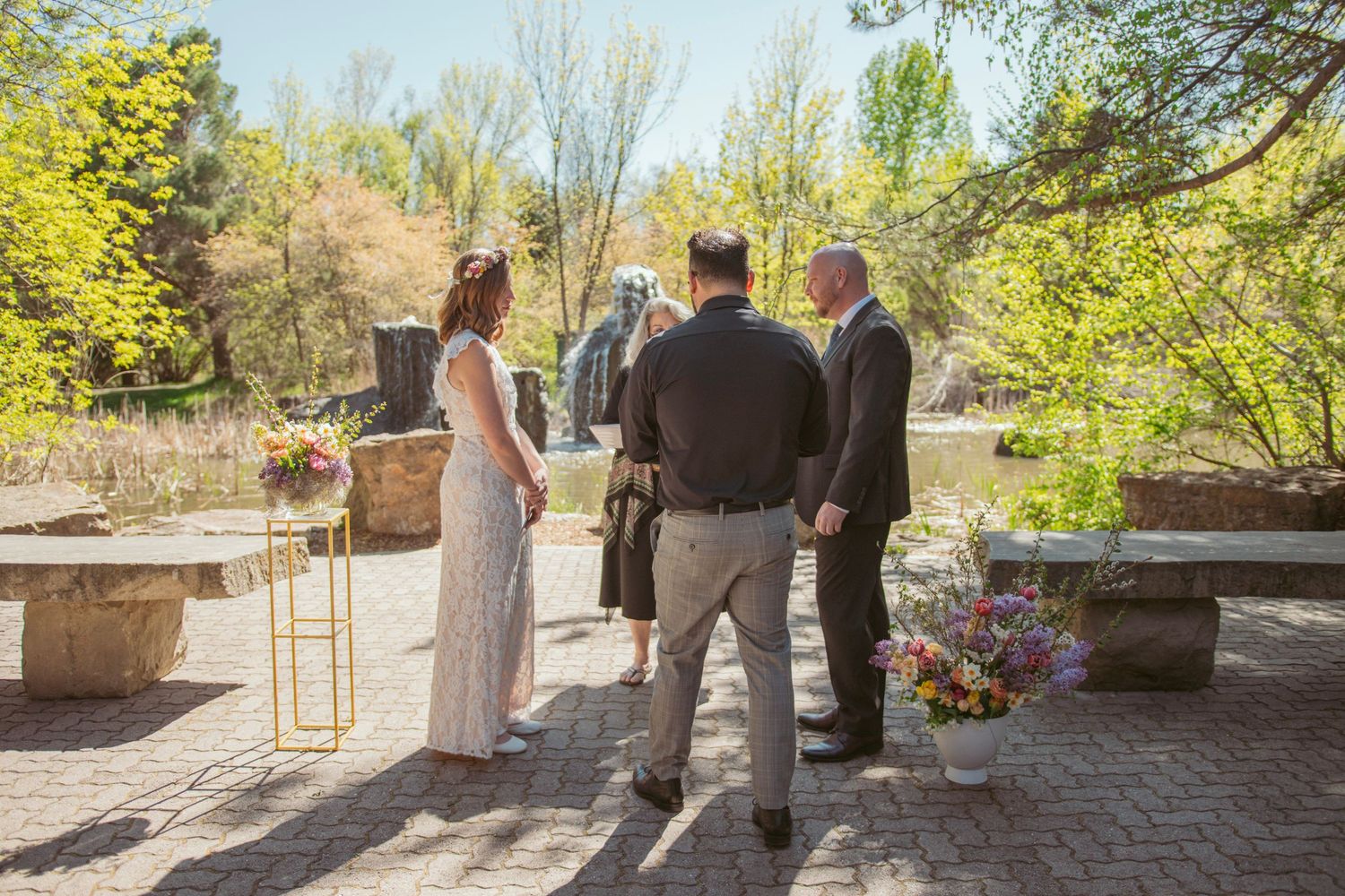 Garden wedding ceremony with guests seated beneath a wooden pergola surrounded by spring foliage.